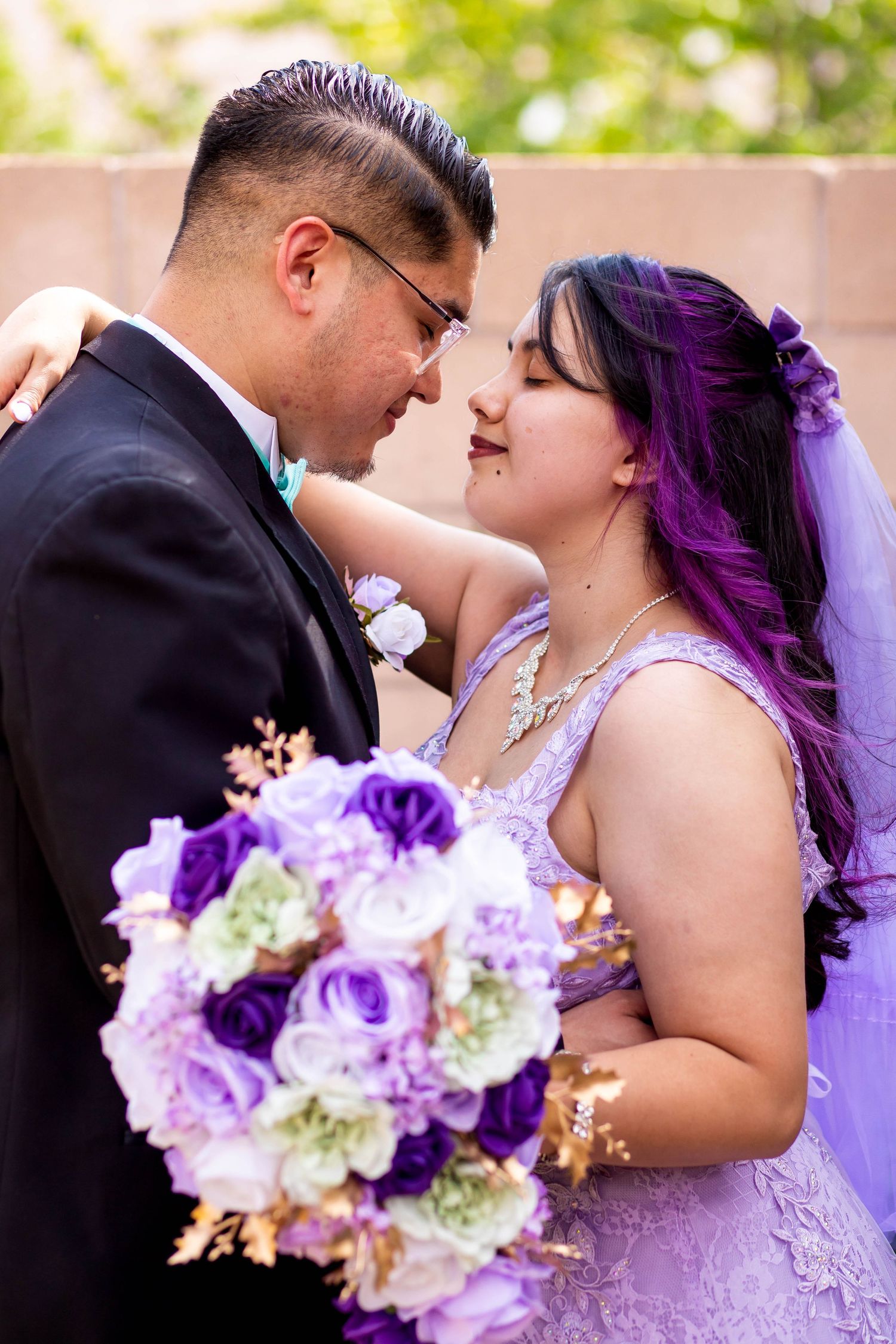 Bride with purple hair holds bouquet while sharing tender moment with groom.