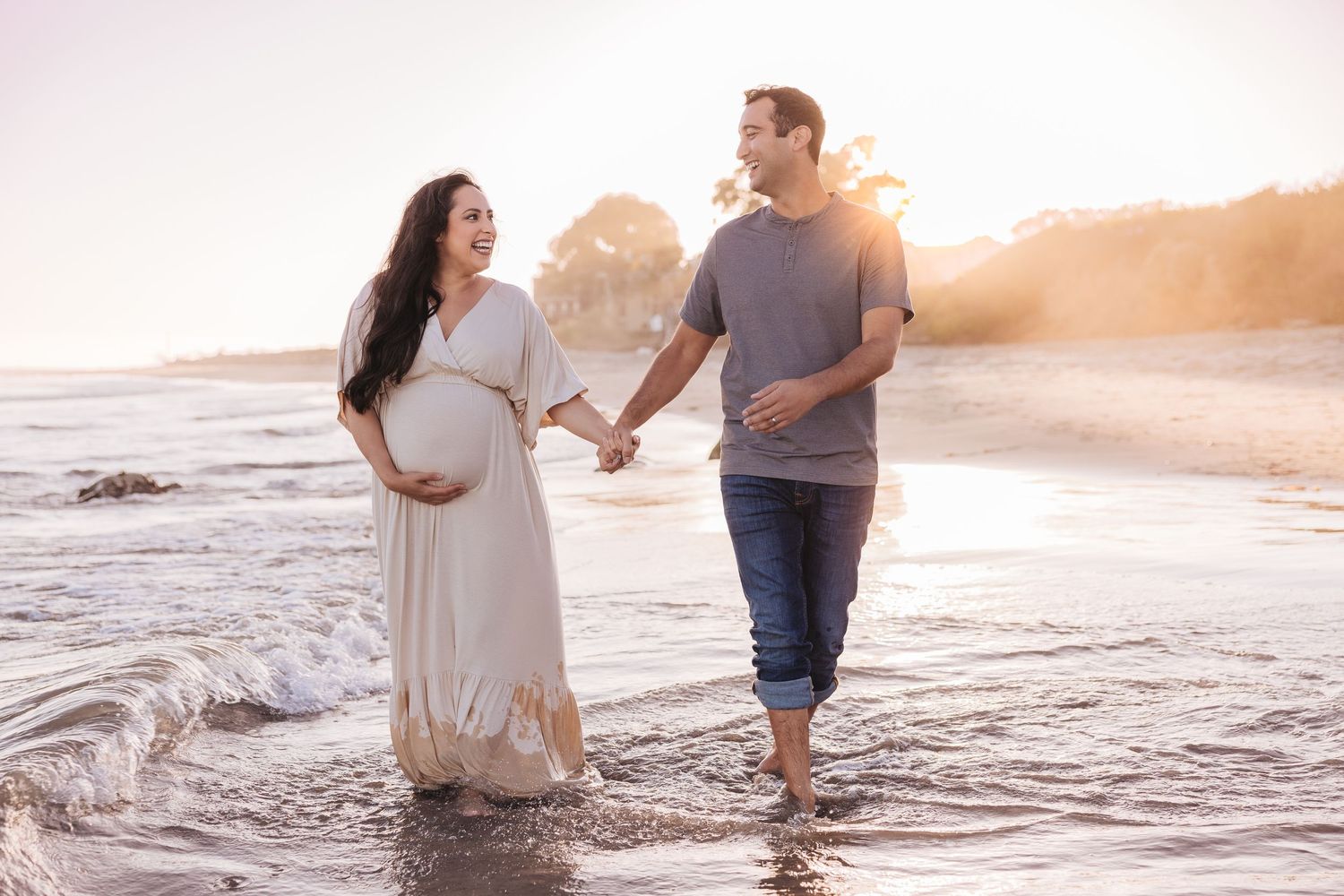 Romantic beach photoshoot with couple walking through gentle ocean waves at sunset.