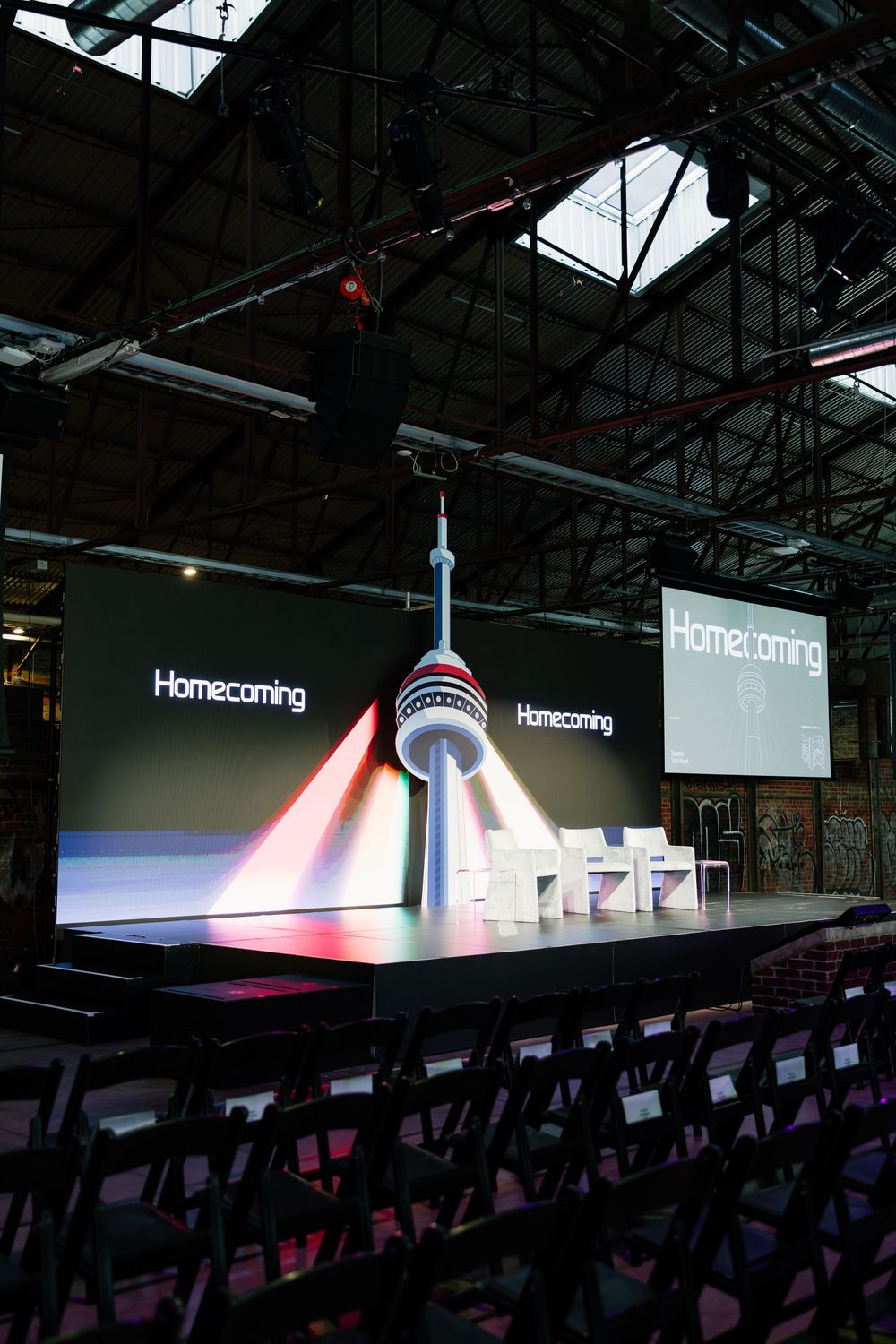 Long view of empty auditorium seating with illuminated Homecoming signage and display lighting on stage.