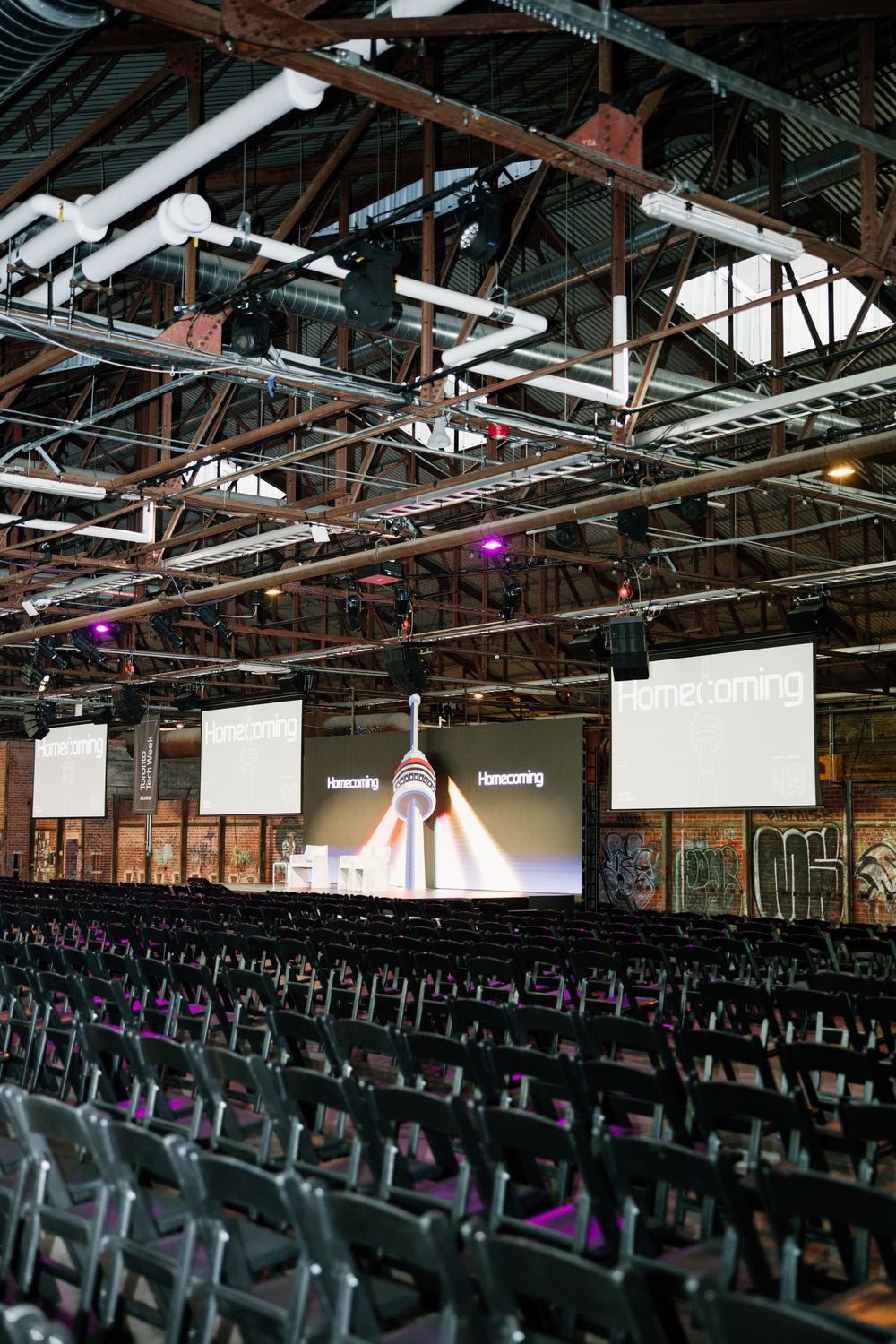 Large conference venue with rows of empty chairs and multiple screens displaying content on stage.