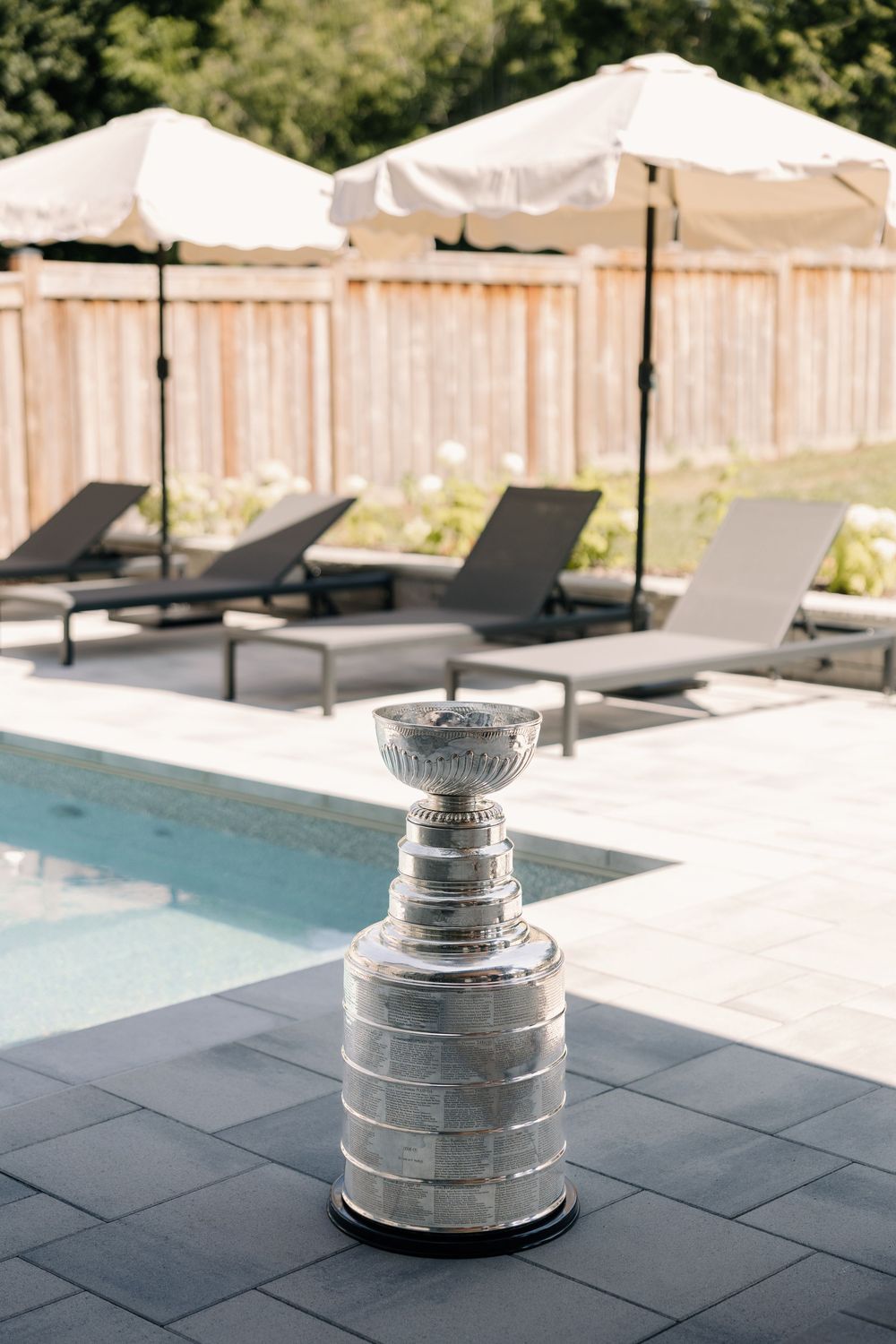 Stanley Cup trophy displayed poolside with lounge chairs and umbrellas in background.