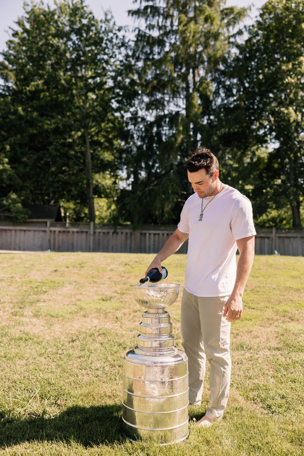 Man pouring champagne into the Stanley Cup trophy on a green lawn outdoors.
