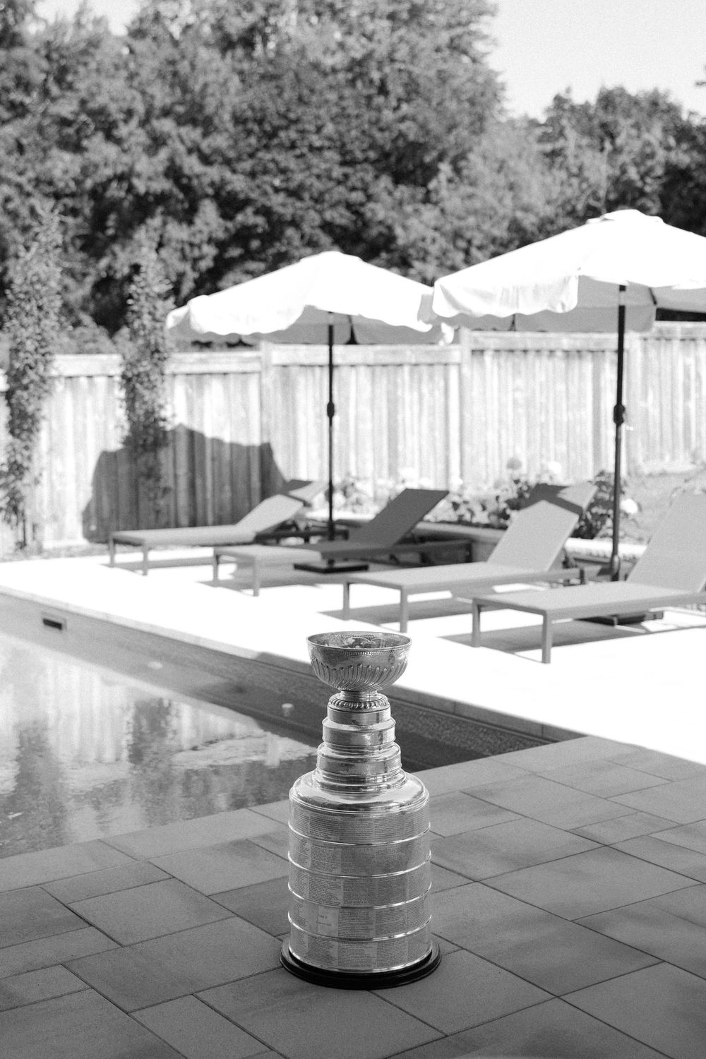 Stanley Cup trophy displayed poolside with lounge chairs and umbrellas in a luxurious backyard setting.