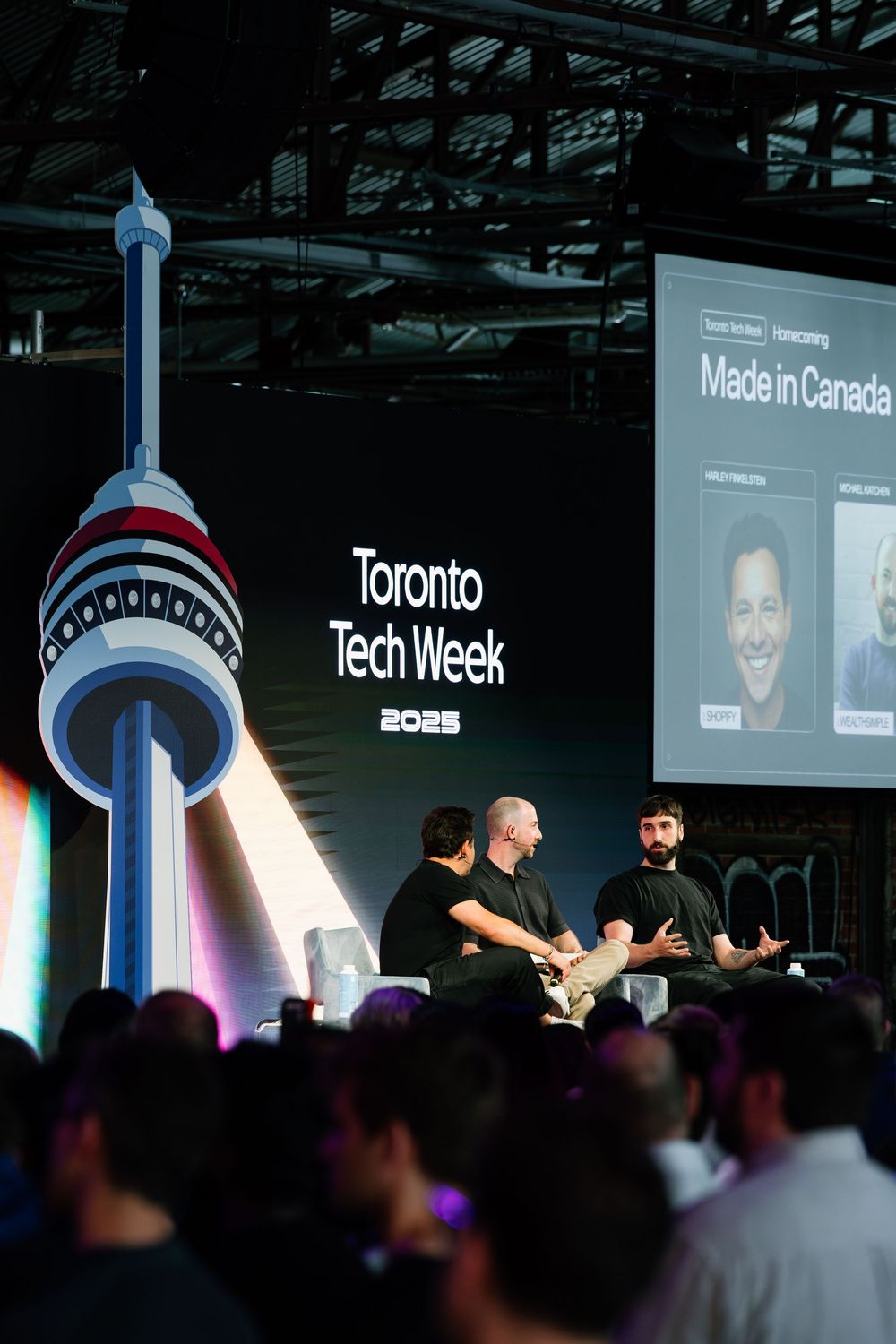 Conference speakers engage with audience during presentation at Toronto Tech Week event with illuminated CN Tower backdrop.