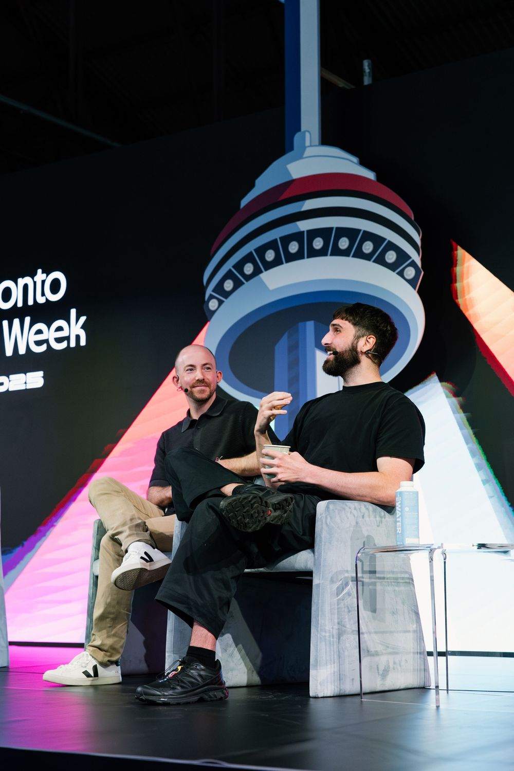 Two speakers engage in discussion on stage at Toronto Tech Week with the CN Tower logo displayed in the background.