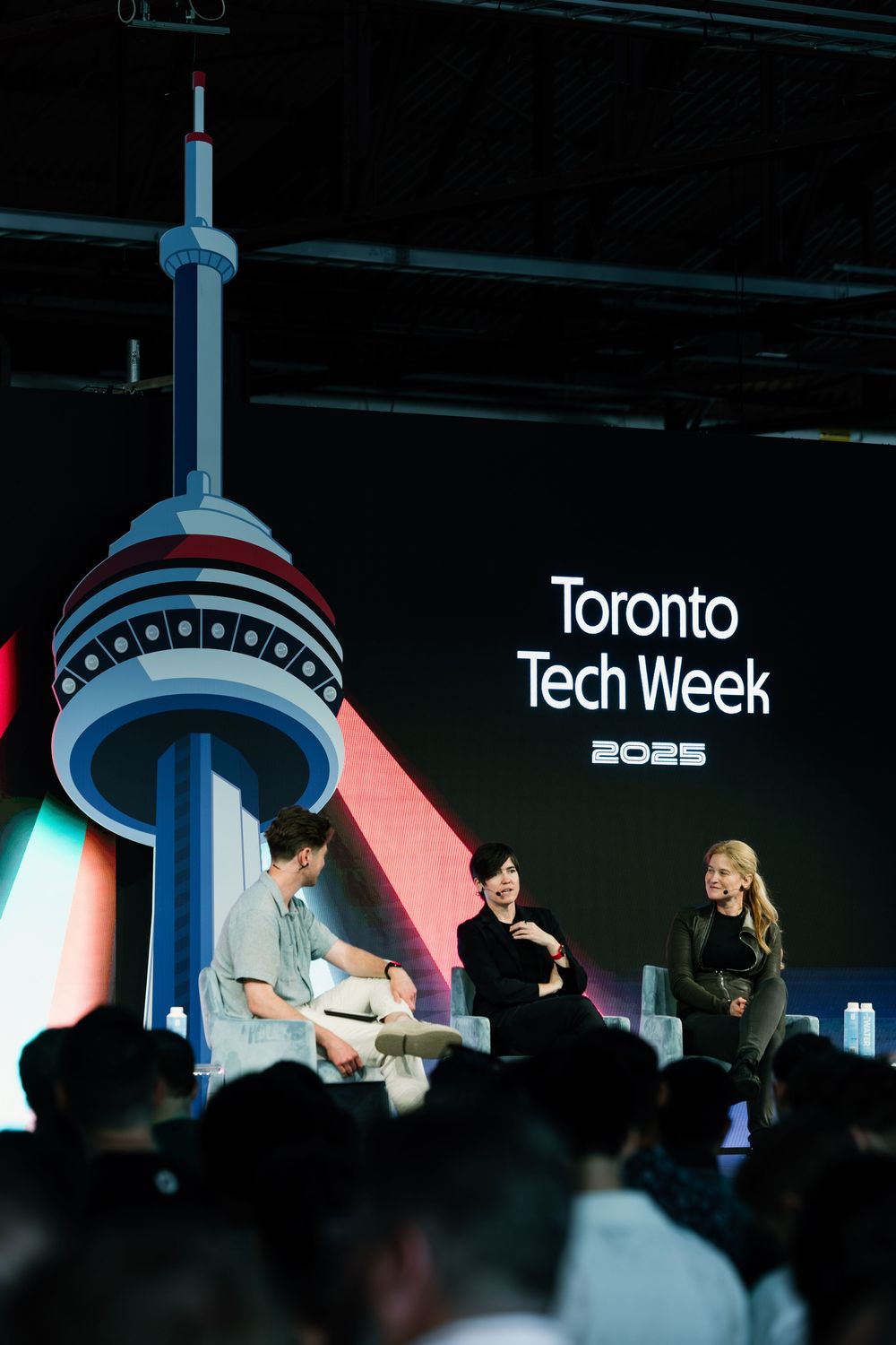Speakers on stage at Toronto Tech Week 2025 with iconic CN Tower silhouette glowing in background during panel discussion.