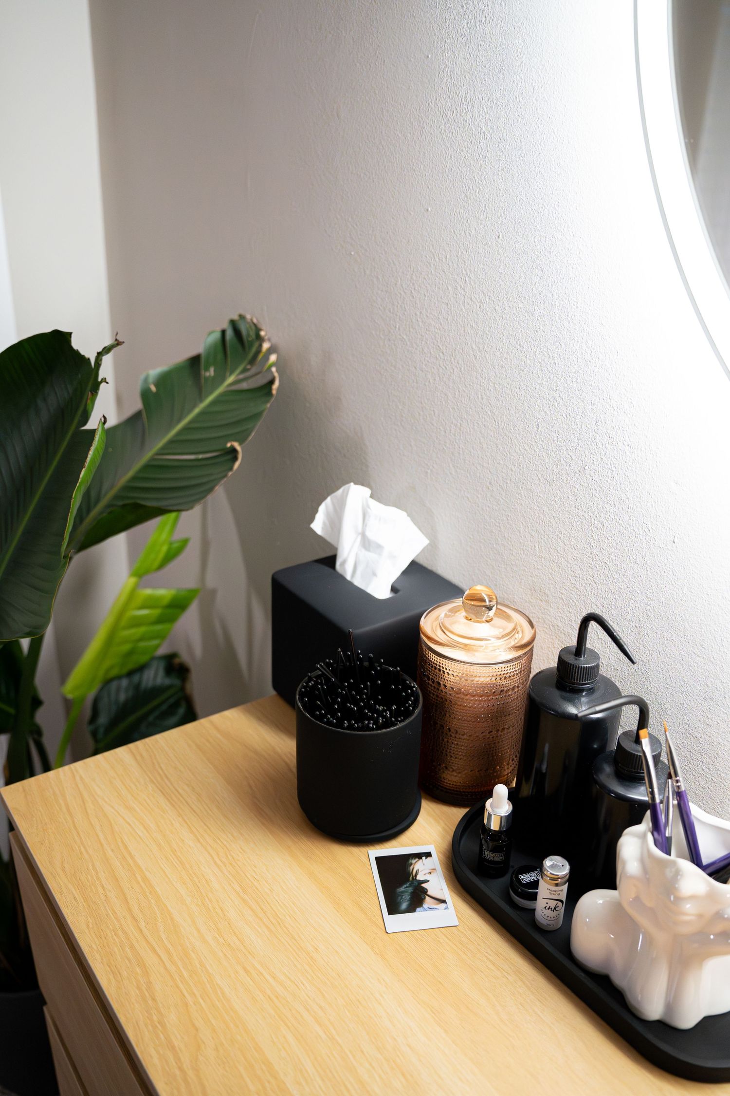 Minimalist vanity setup with tissue box, candle, and self-care items on wooden surface near plant.