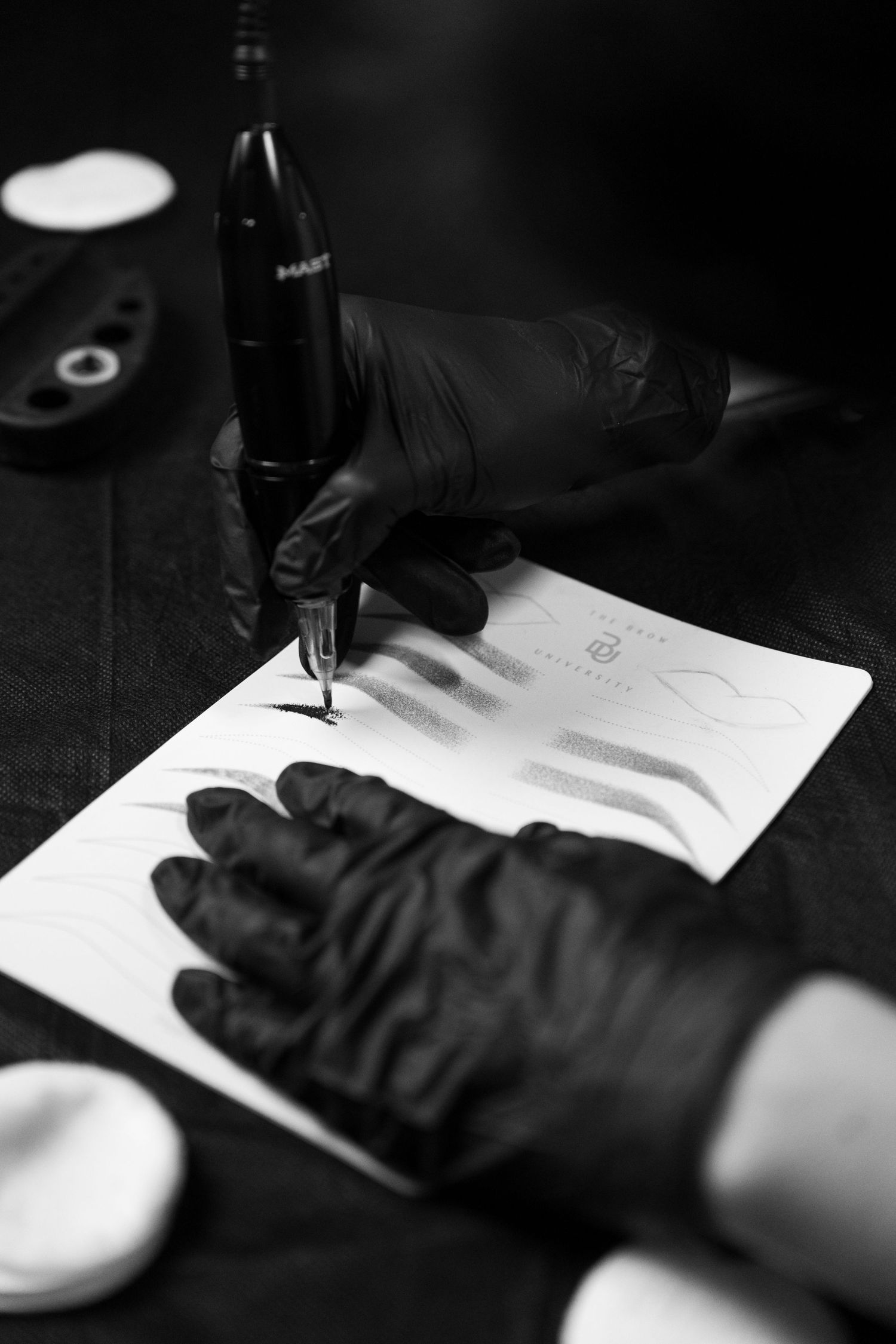 Hands wearing black gloves writing on practice pad for permanent makeup training.