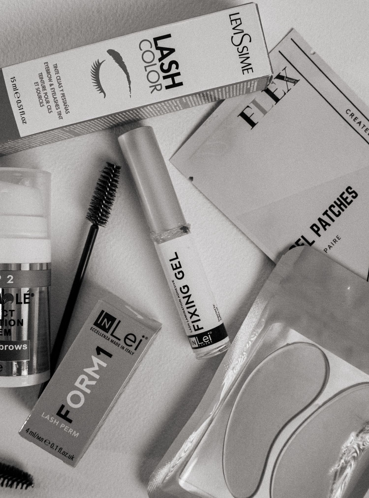 Collection of beauty and cosmetic products including lash enhancers and skincare items in black and white tones.