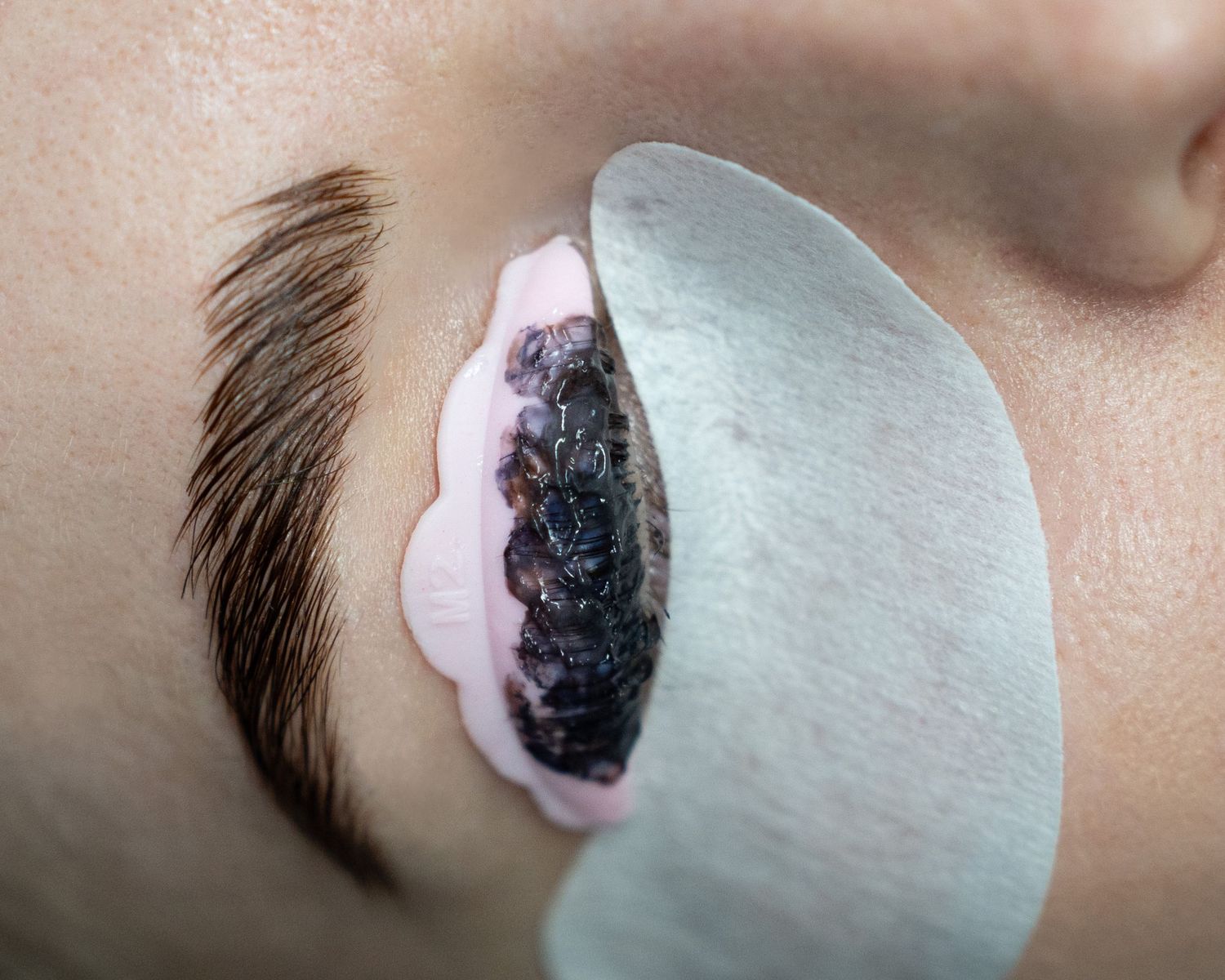 Extreme close-up of an eyelash extension application with protective under-eye pad.