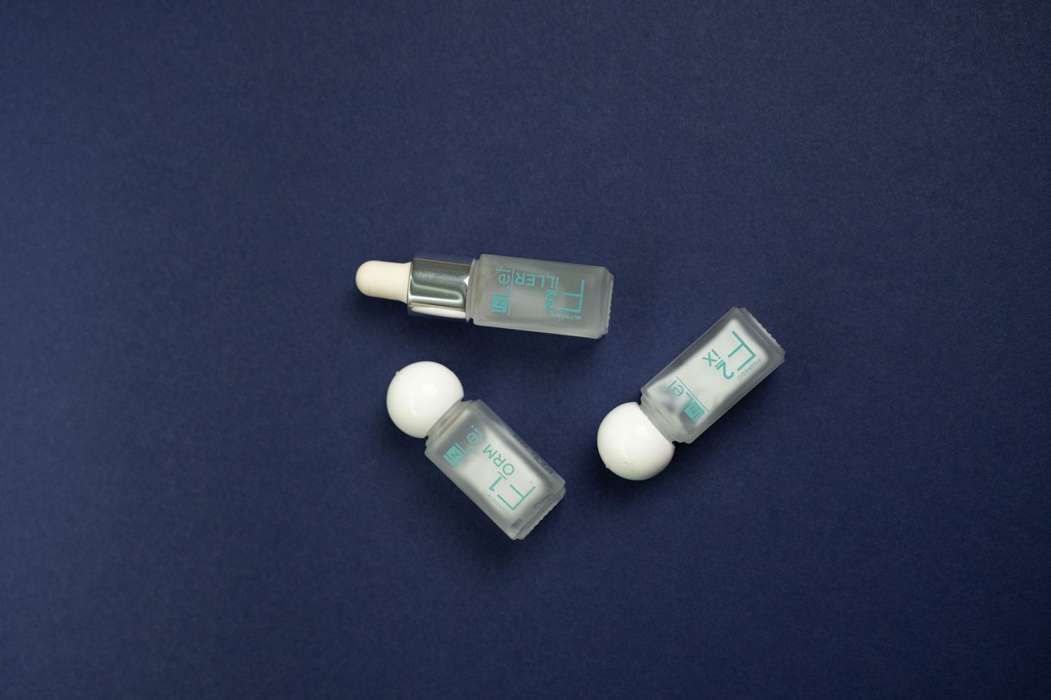 Three small glass vials with white dropper caps against a navy blue background.