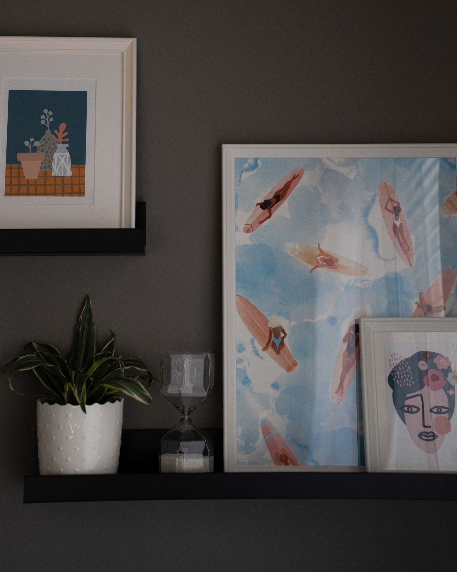 Wall shelf decorated with framed artwork featuring swimming figures and a potted plant.