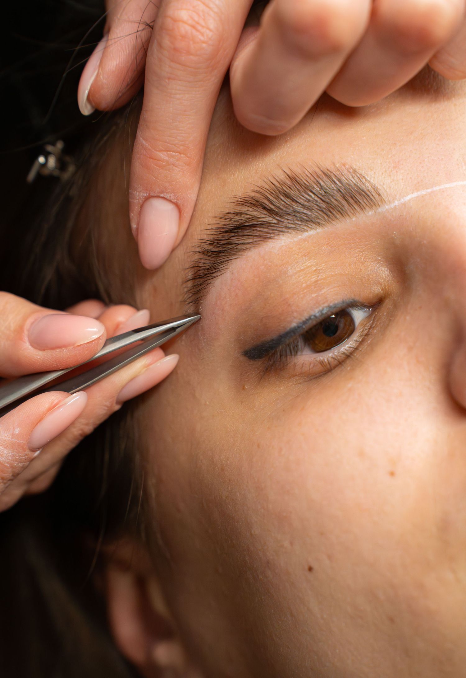 Close-up of eyebrow grooming technique using precise tweezing tools.