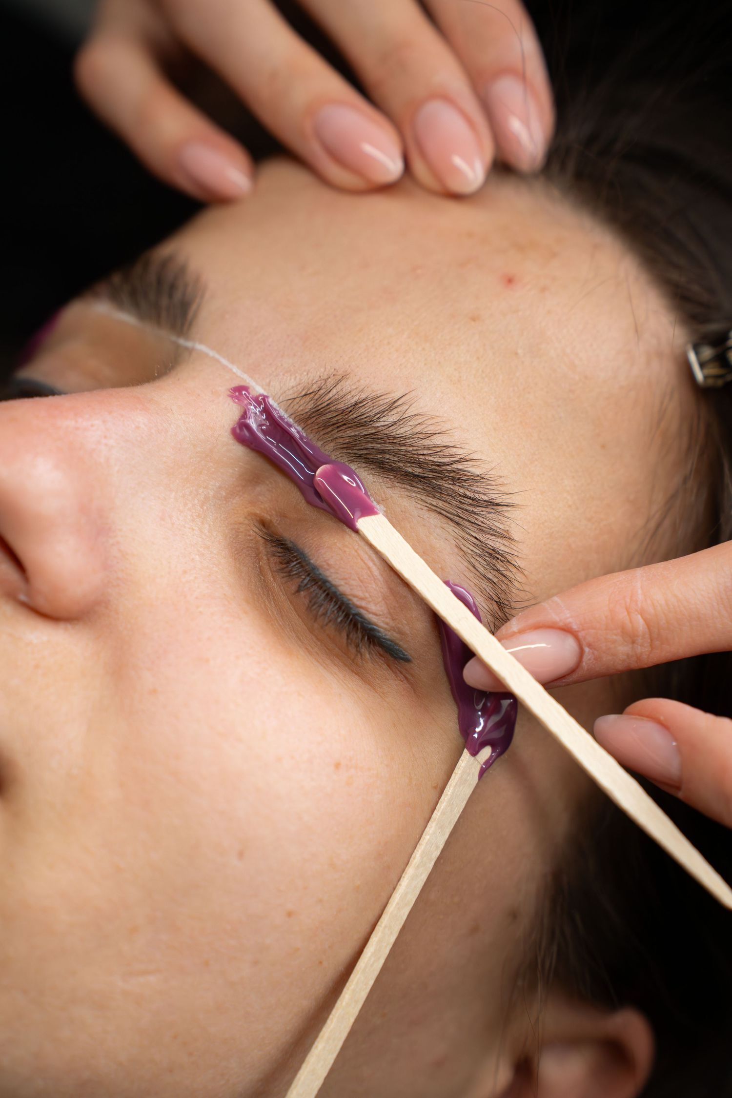 Detailed view of eyebrow grooming procedure using disposable brushes and tools.