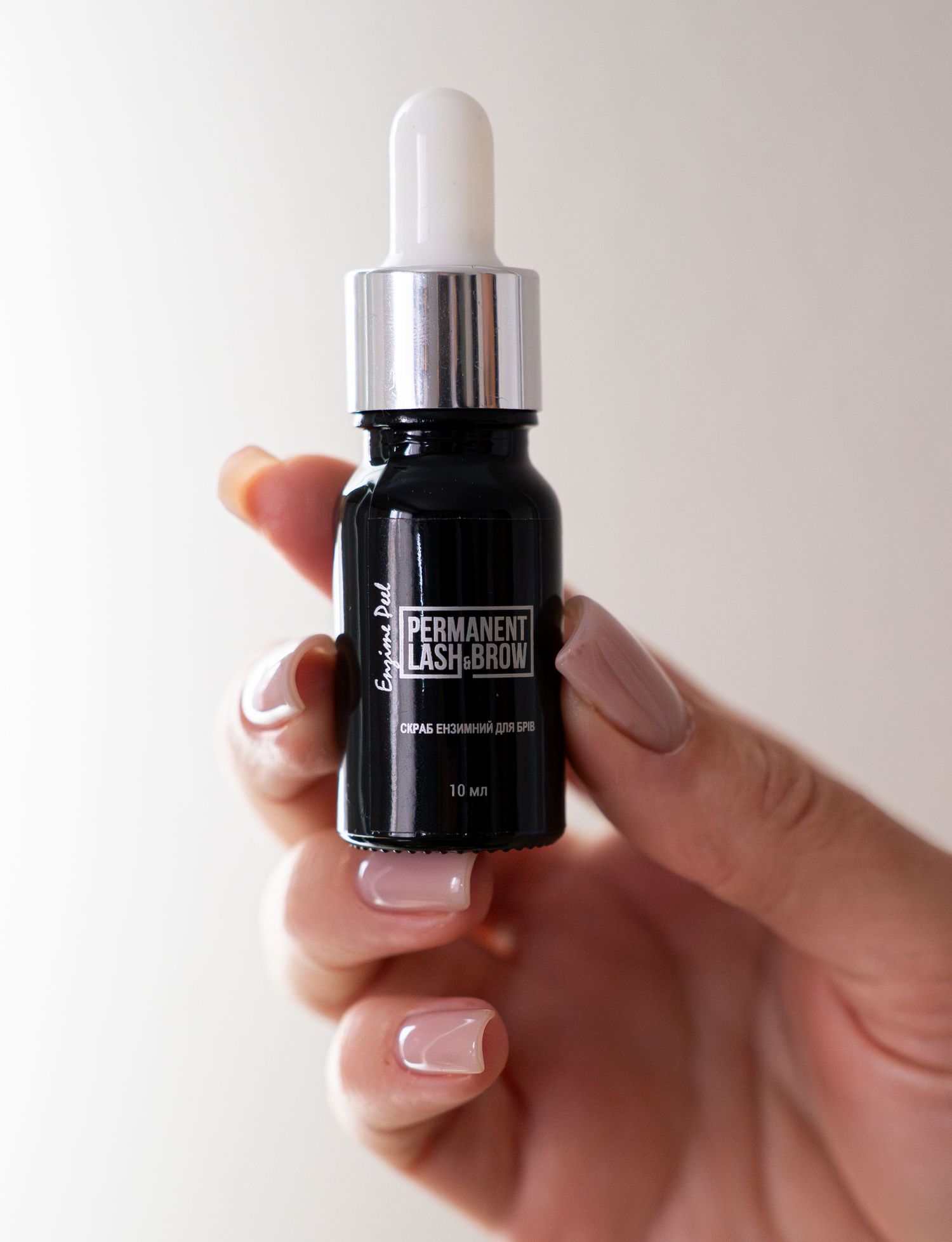 Hand holding a black dropper bottle of beauty serum against white background.