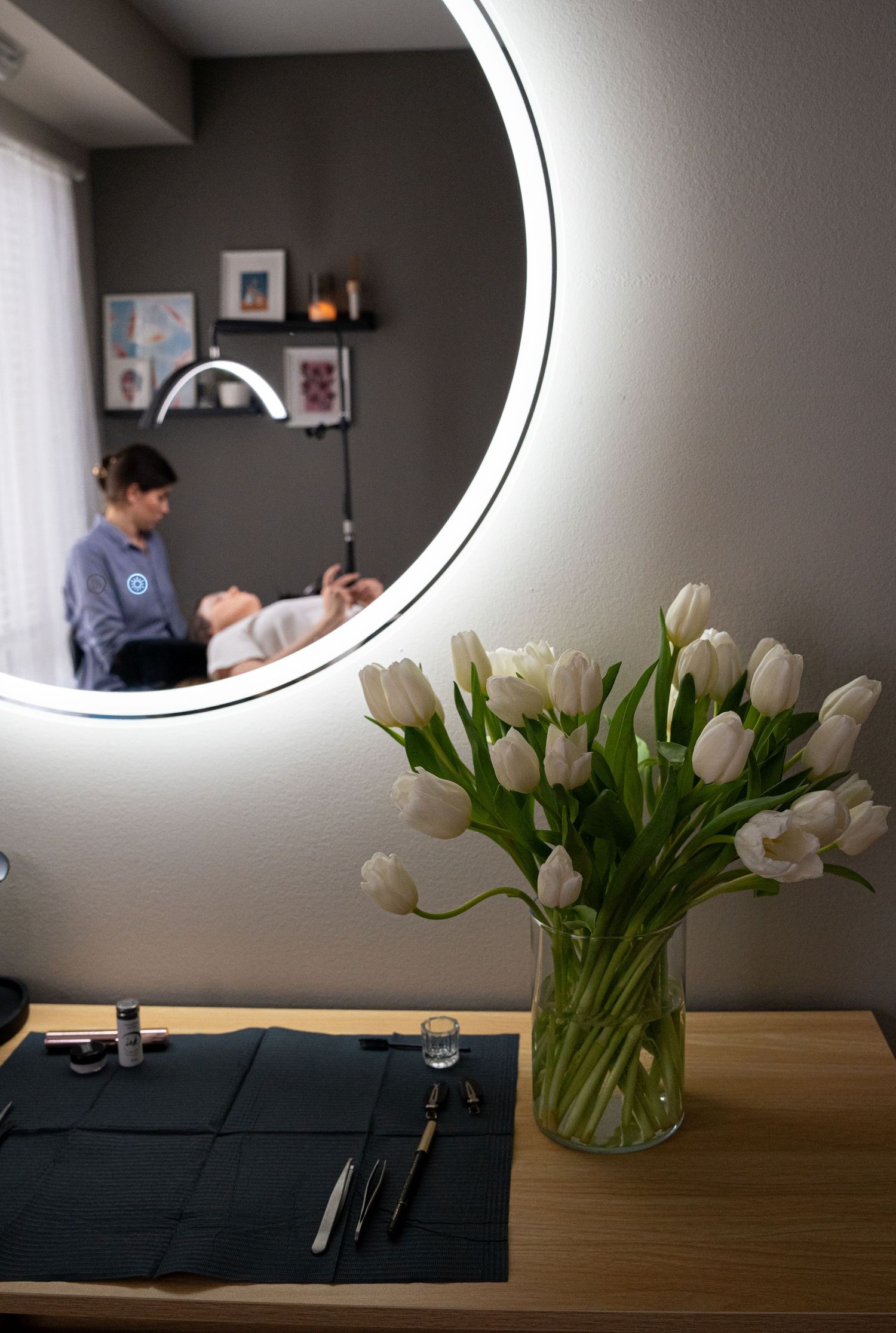 Reflection in round mirror showing beauty treatment room with white tulips in foreground.