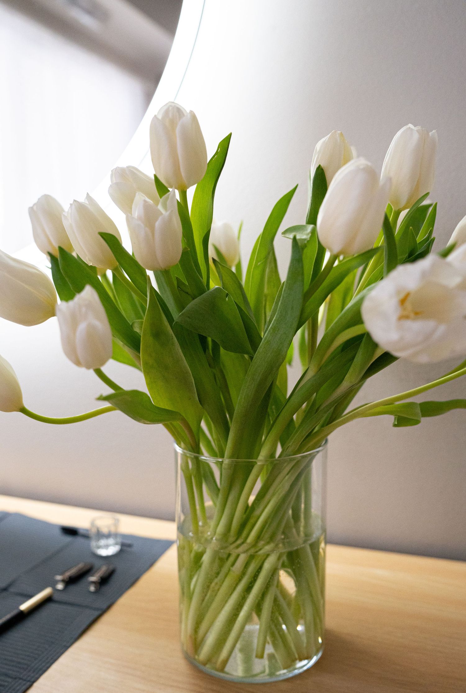 Fresh white tulips arranged in a clear glass vase with bright green stems.