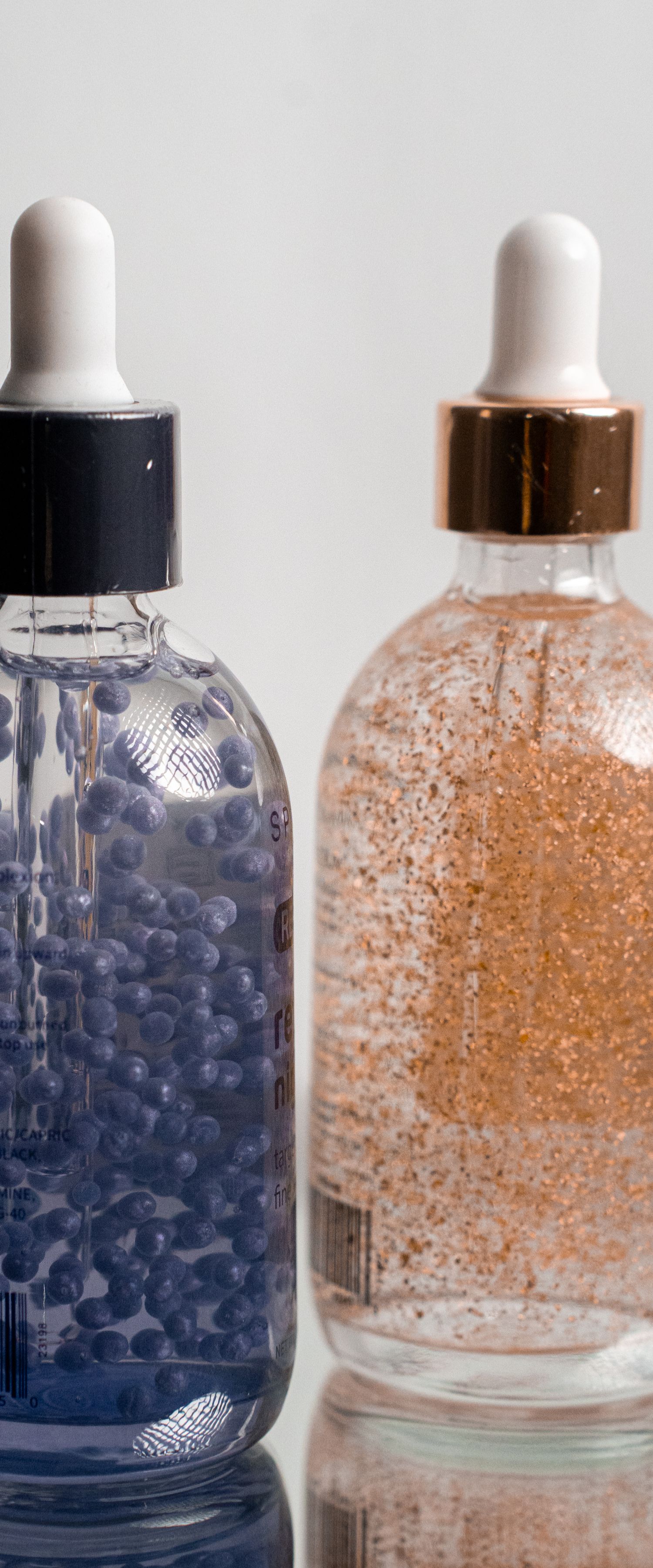 Two glass dropper bottles containing skincare serums with blue and rose gold shimmer particles.