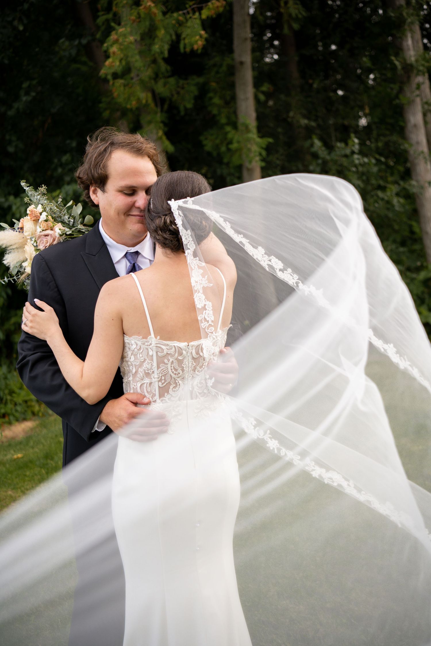 A close-up detail shot of embracing newlyweds showing the intricate lace wedding dress. Farmhill Weddings