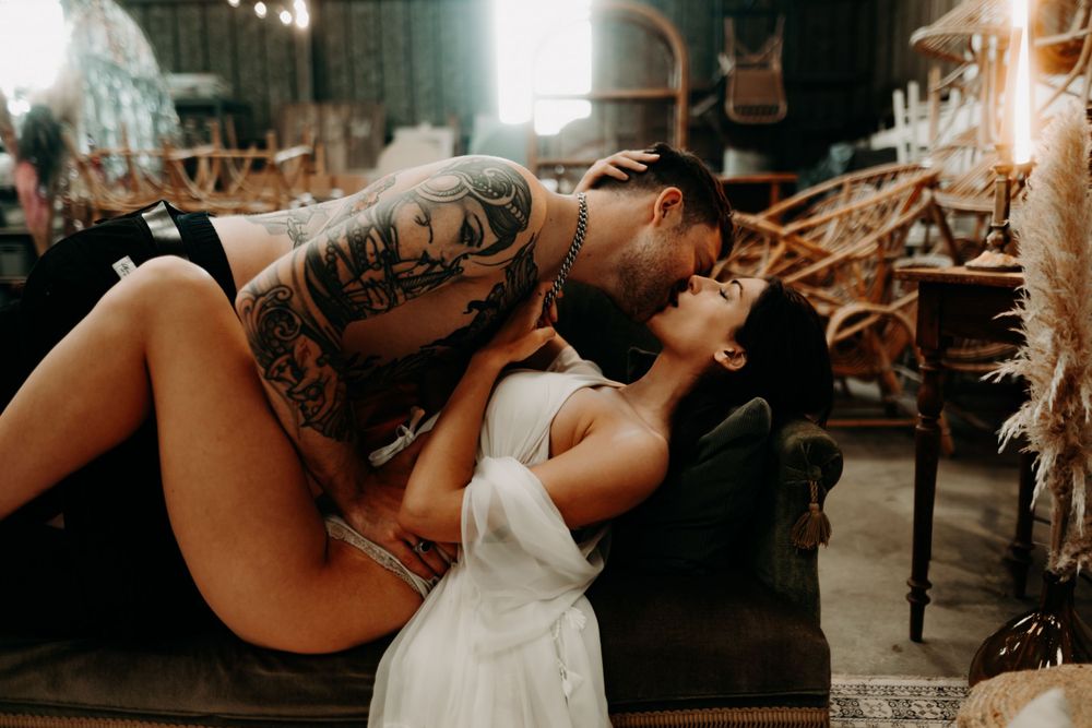 A couple dressed in black and white share a romantic kiss in an atmospheric indoor setting with moody lighting.