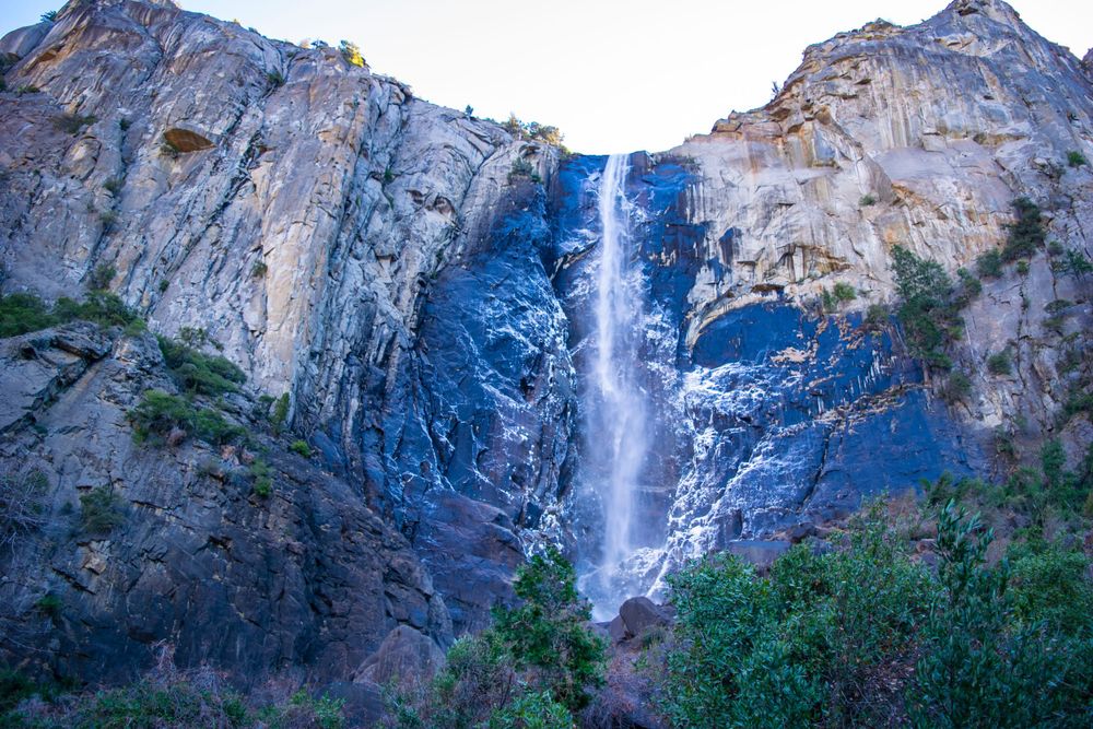 Bridalveil Falls flows down massive granite cliff face during blue hour in Yosemite National Park.