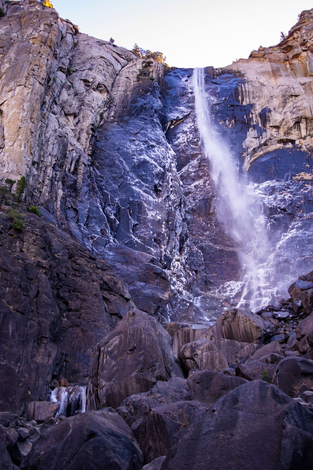 Dramatic waterfall plunges down towering rock face with scattered boulders at base.