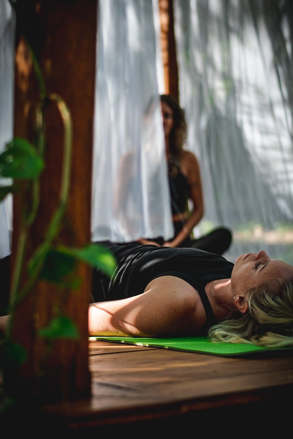 Person lying on yoga mat during relaxation practice in tropical indoor setting.