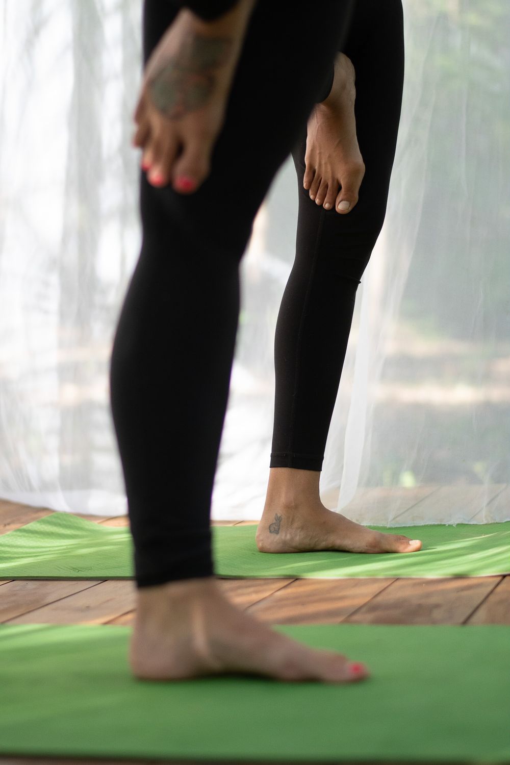 Close-up view of feet in black leggings on a green yoga mat.
