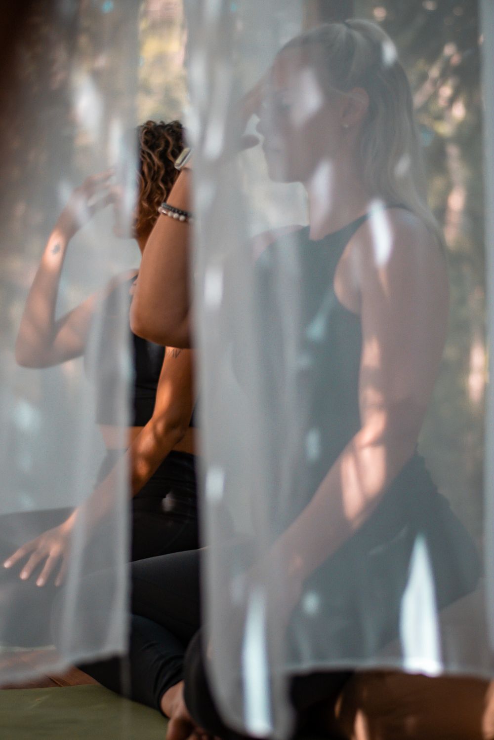 Silhouetted figure in athletic wear seen through sheer curtains during yoga practice.