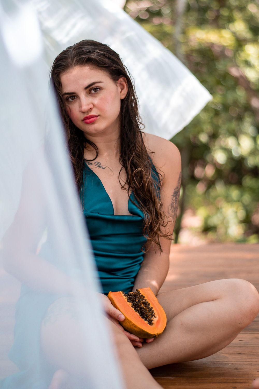 Person in teal dress holding a papaya fruit against white fabric outdoors.
