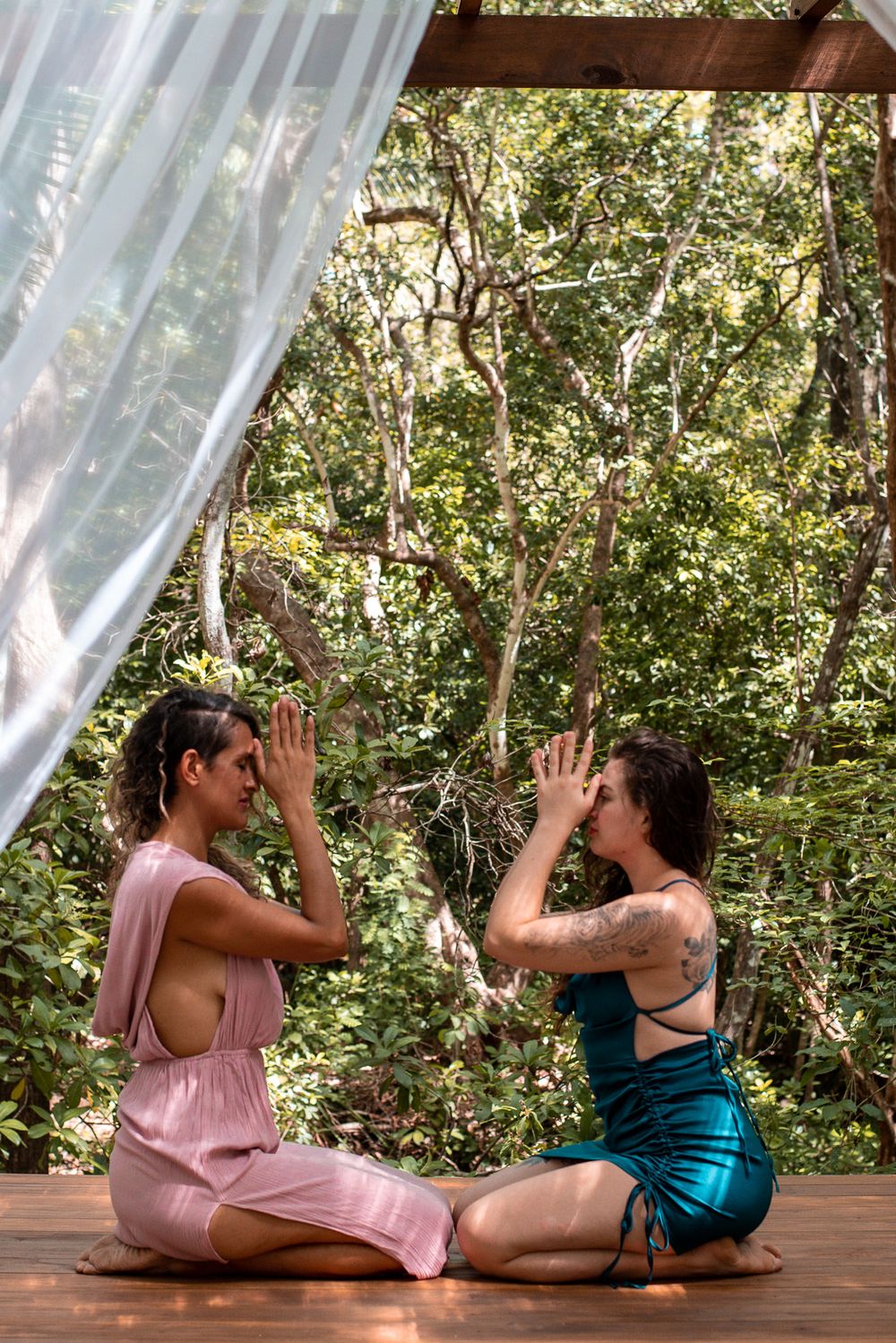 Two people in dresses sitting on wooden deck performing ritual movements.