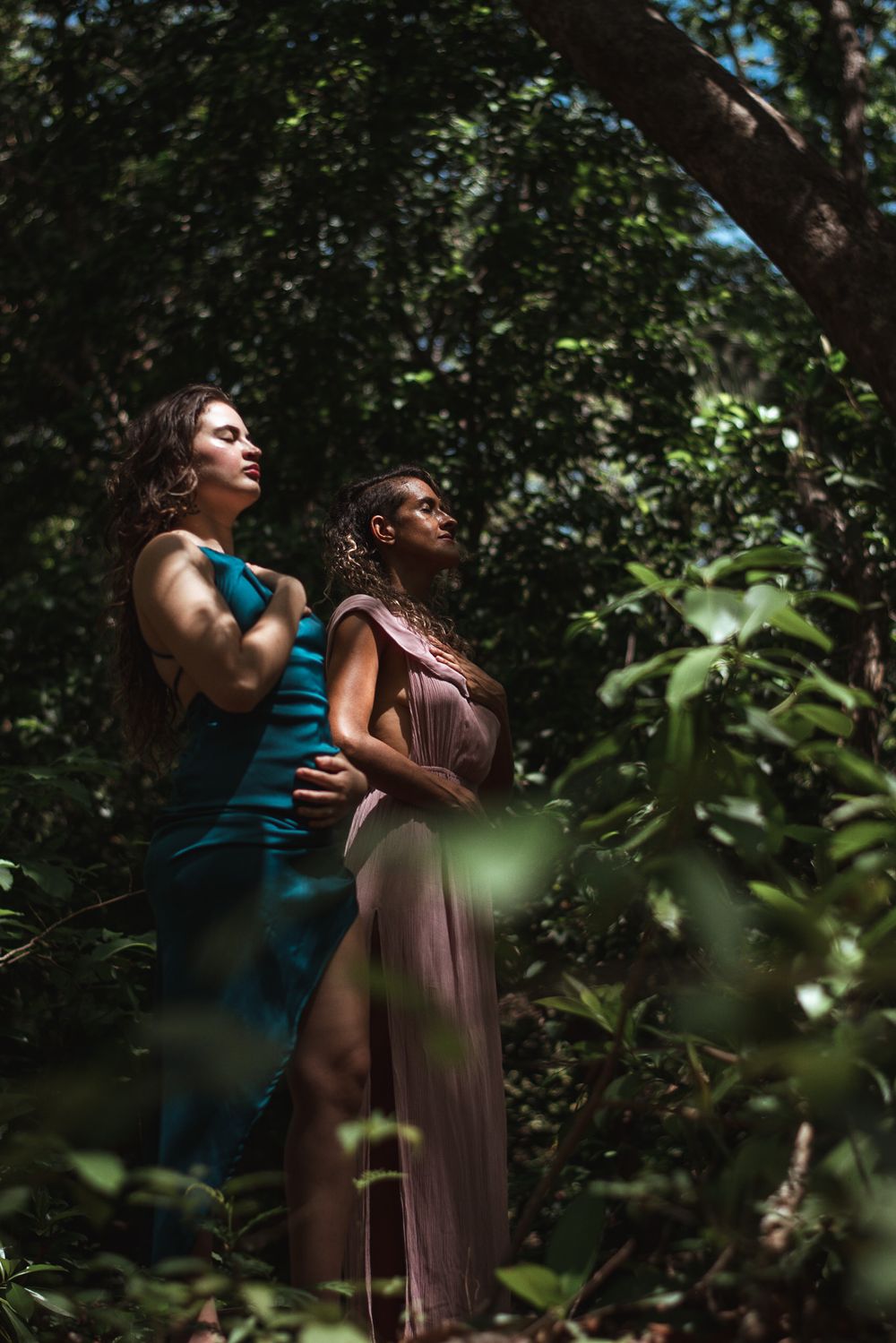 Two figures in flowing dresses standing among lush forest trees.