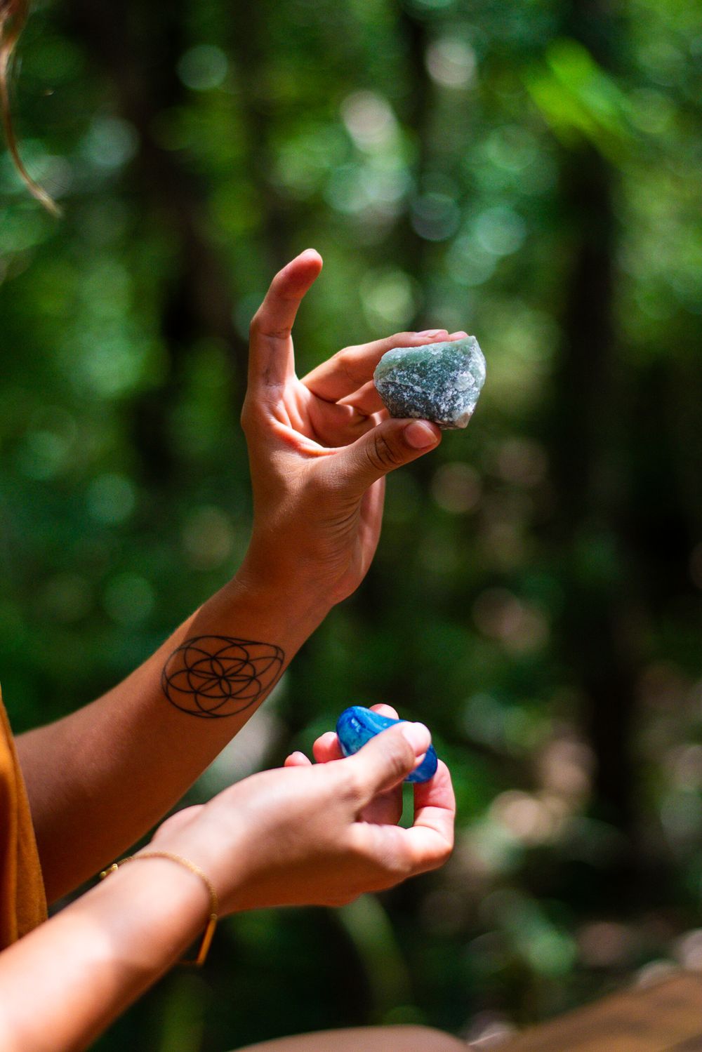 Hands holding crystals with geometric tattoo visible against blurred green background.