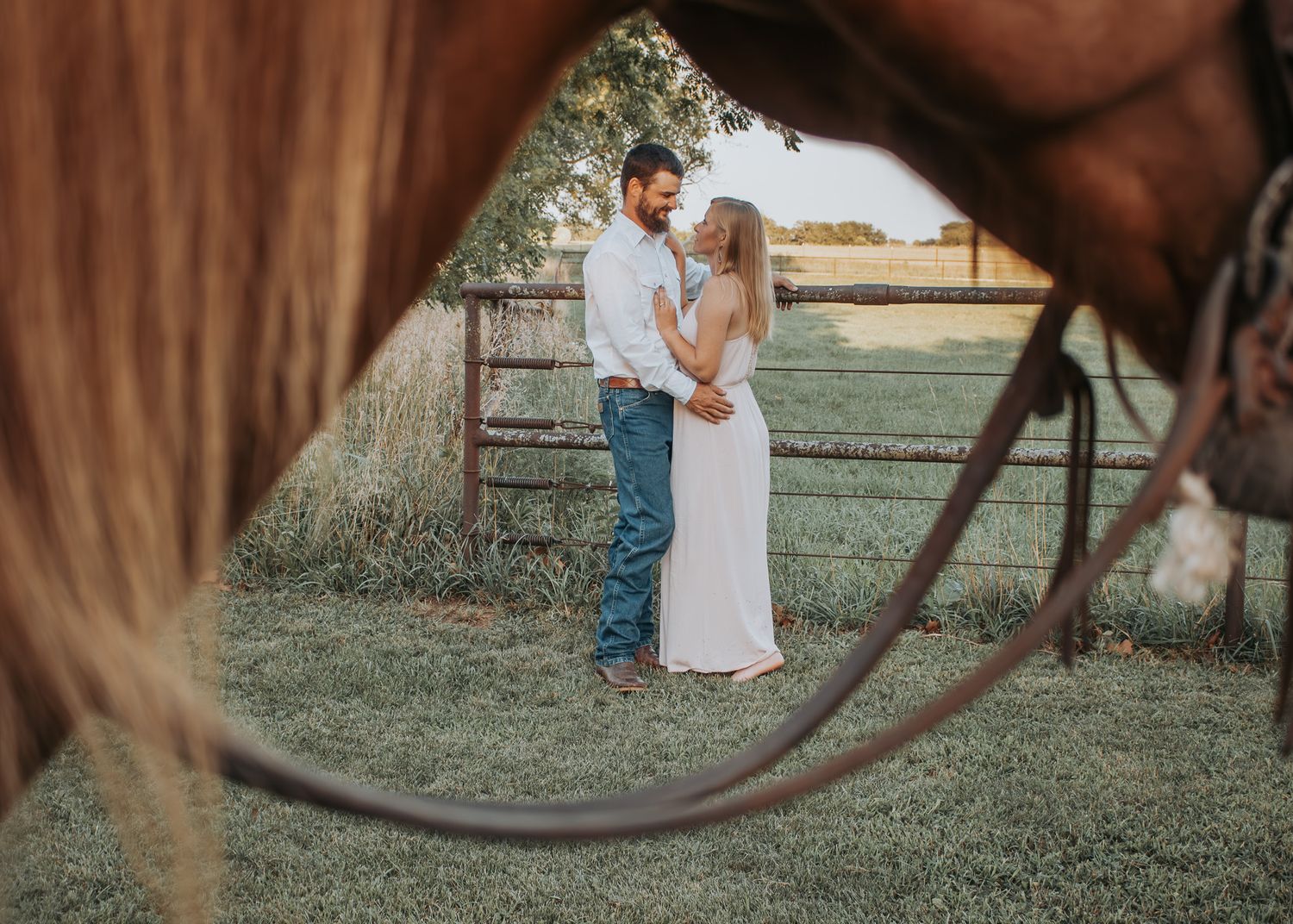 A creative horse bridle framed engagement photo in a summer pasture.