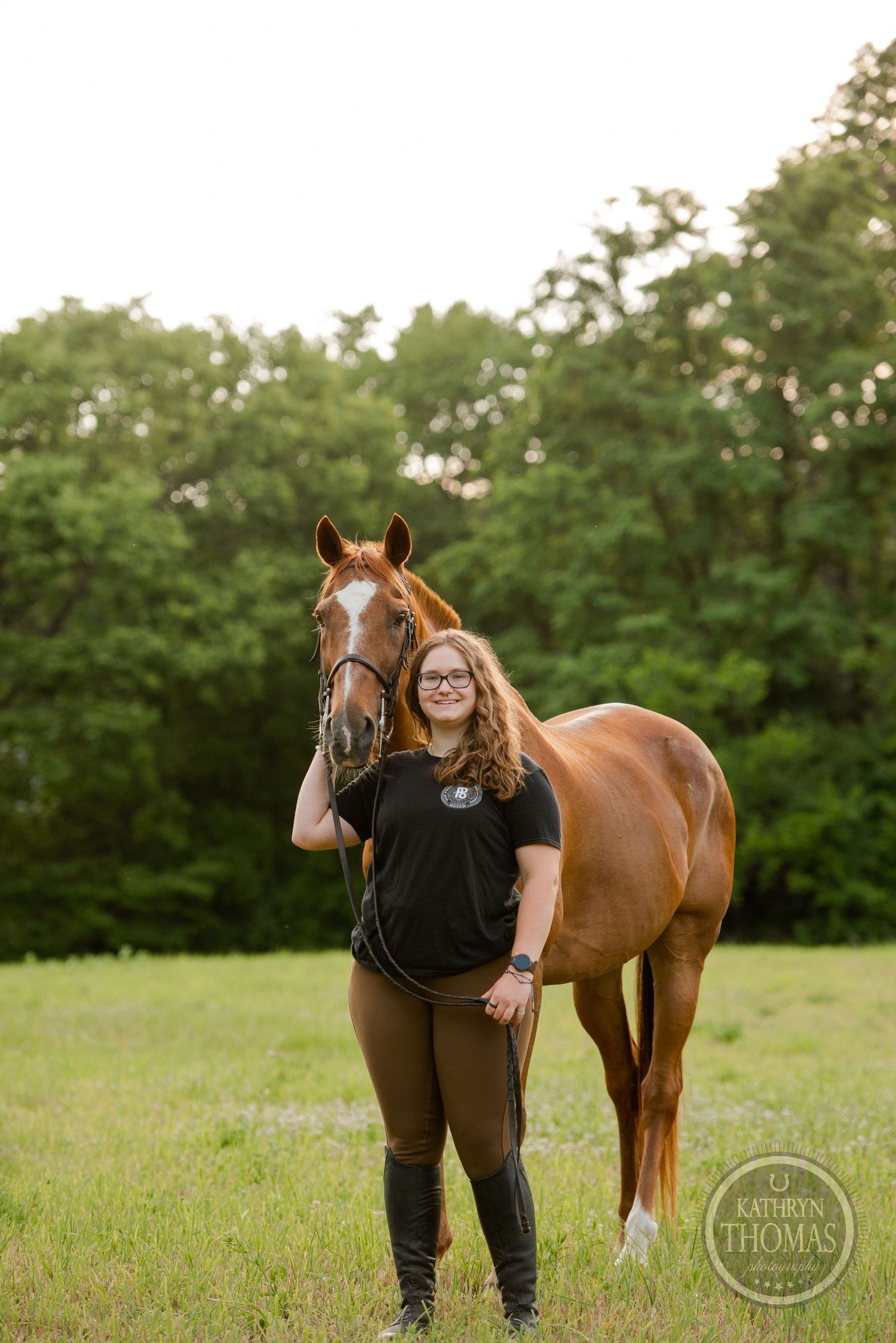 A chestnut horse stands in a grassy field with its handler on a summer evening.
