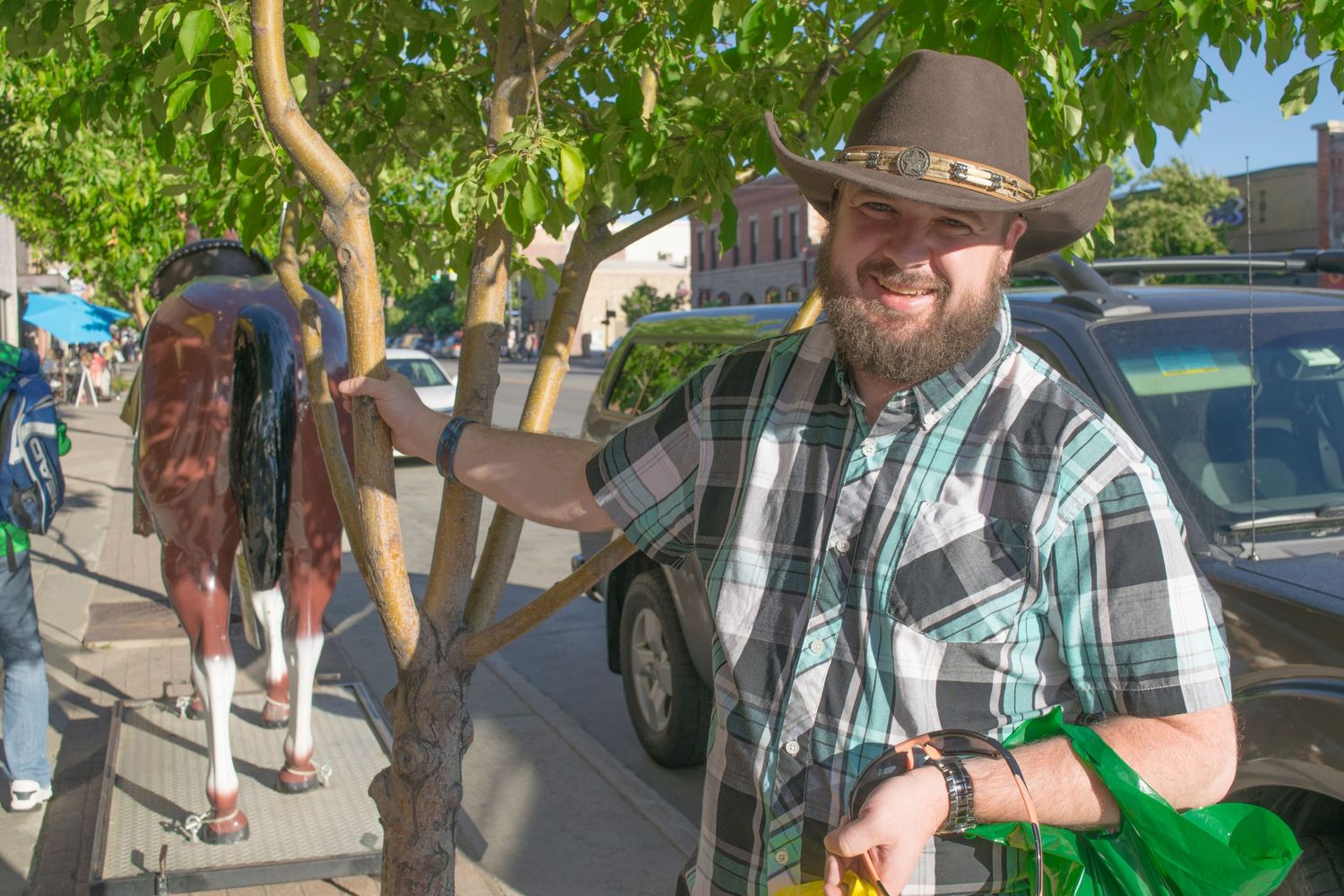 Someone in a brown cowboy hat and plaid shirt standing outdoors on a sunny day.