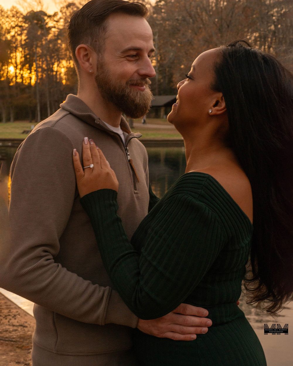 A couple shares an intimate moment at sunset, embracing while wearing sweaters in a warm golden light.