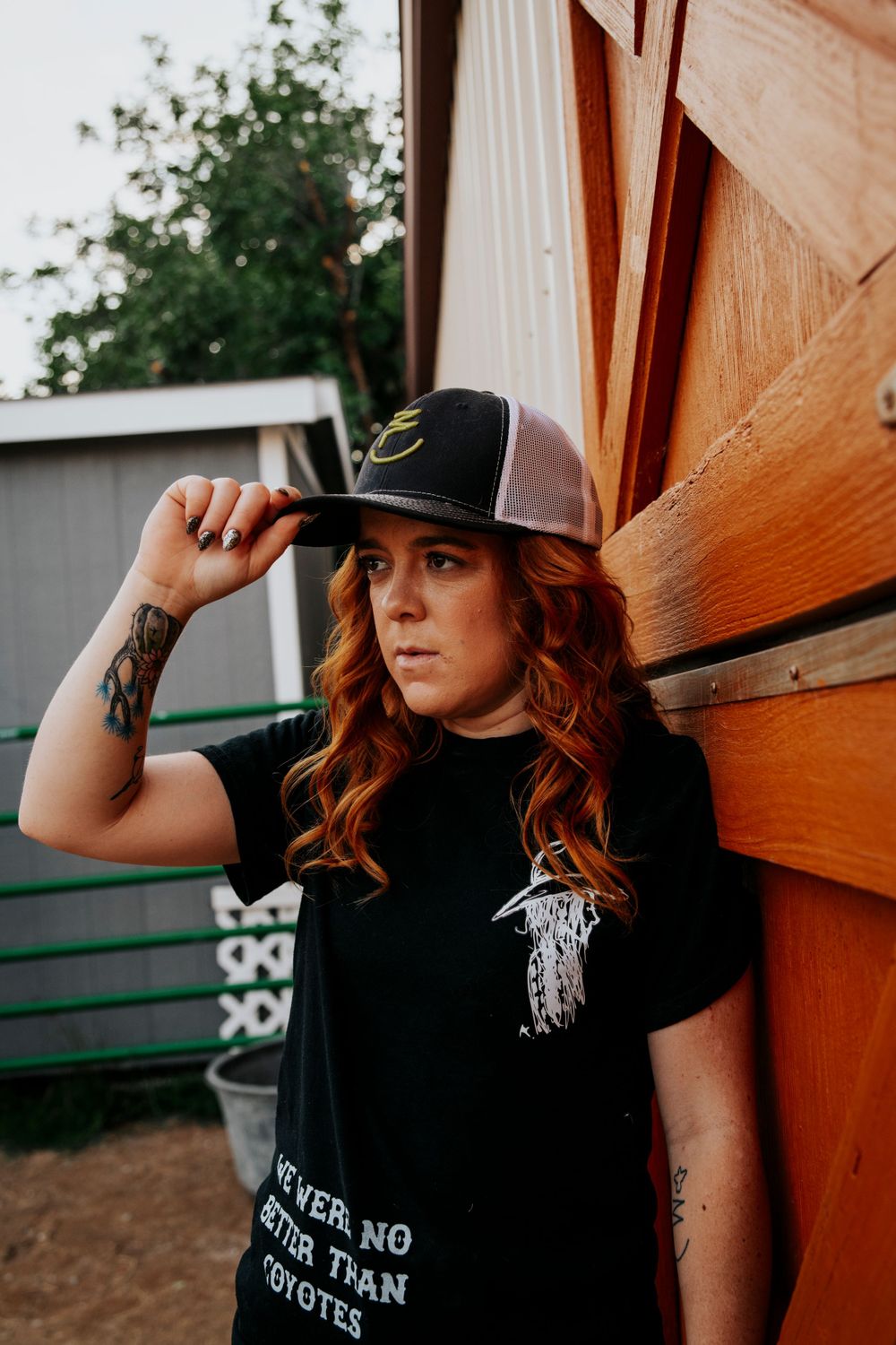 Western style portrait against rustic wooden wall featuring black t-shirt and trucker cap.
