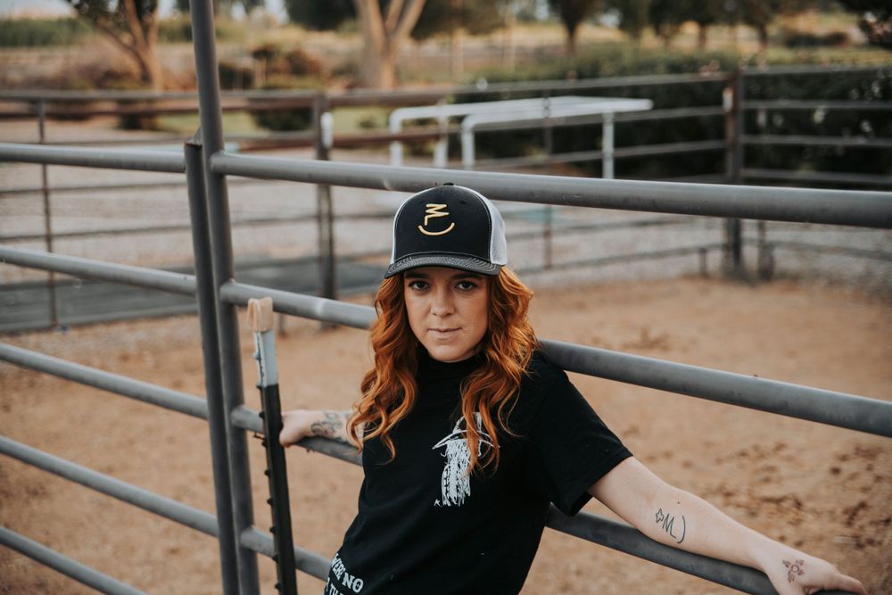Country western style portrait by metal corral fence in outdoor ranch setting.