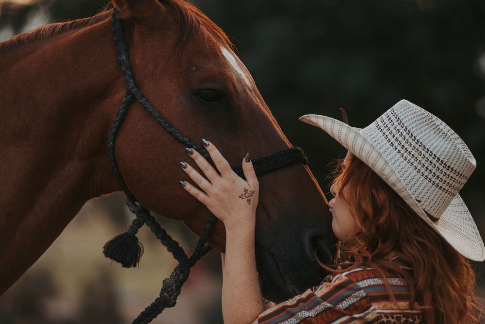 Intimate moment with chestnut horse wearing braided halter in outdoor setting.