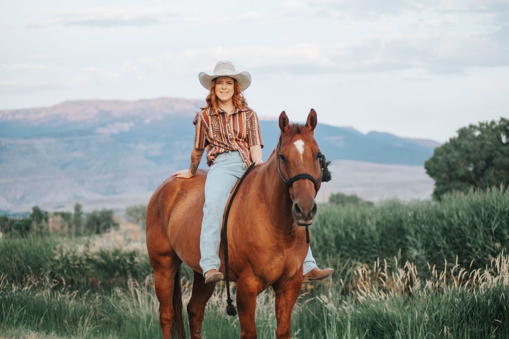 Horseback rider in western attire against mountain landscape.