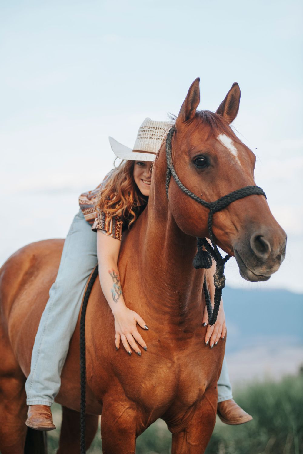 Affectionate moment with chestnut horse against mountain backdrop.