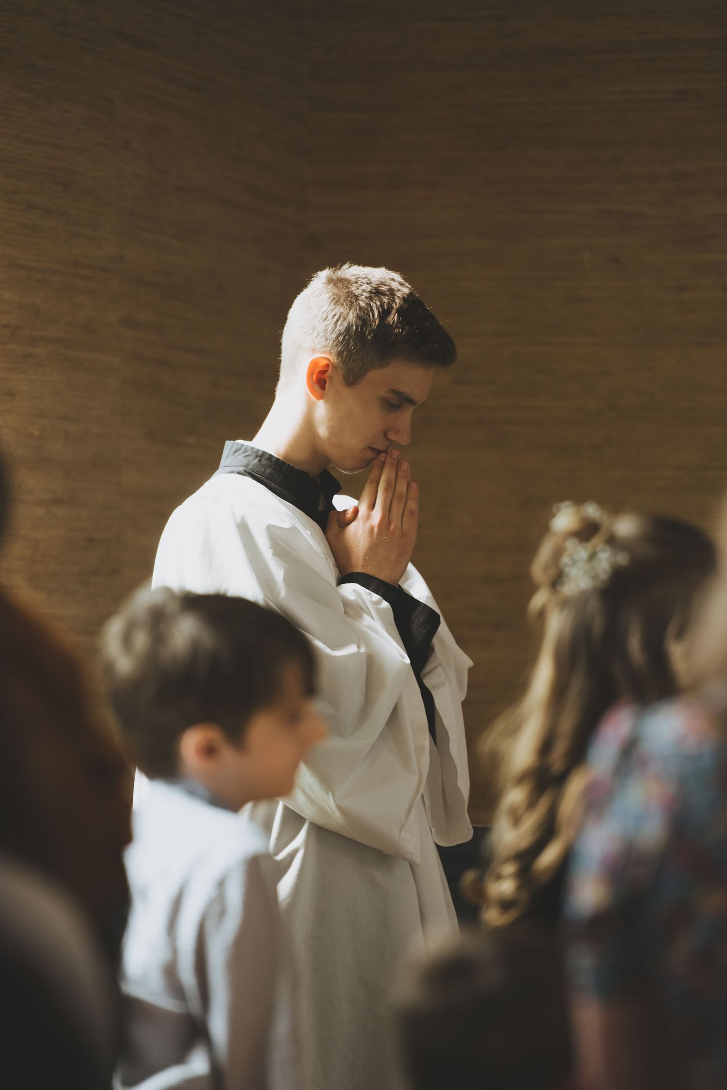 An altar server in white robes stands in prayer during a church service.