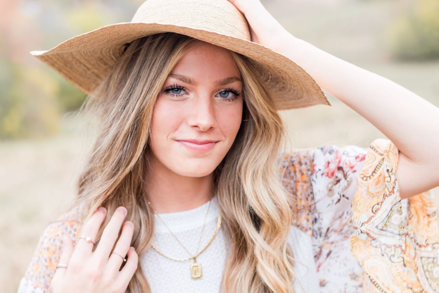 A senior portrait of a girl with a hat smiling at the camera.