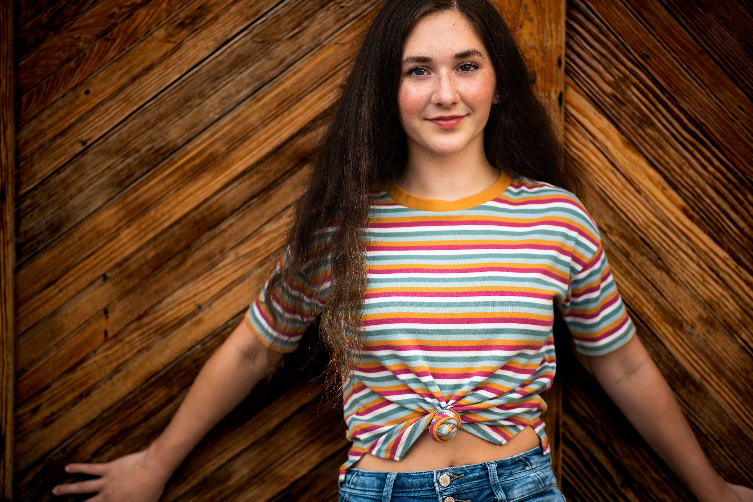 high school senior girl portrait in the west bottoms kansas city missouri against a wooden door wearing a colorful striped shirt and jeans