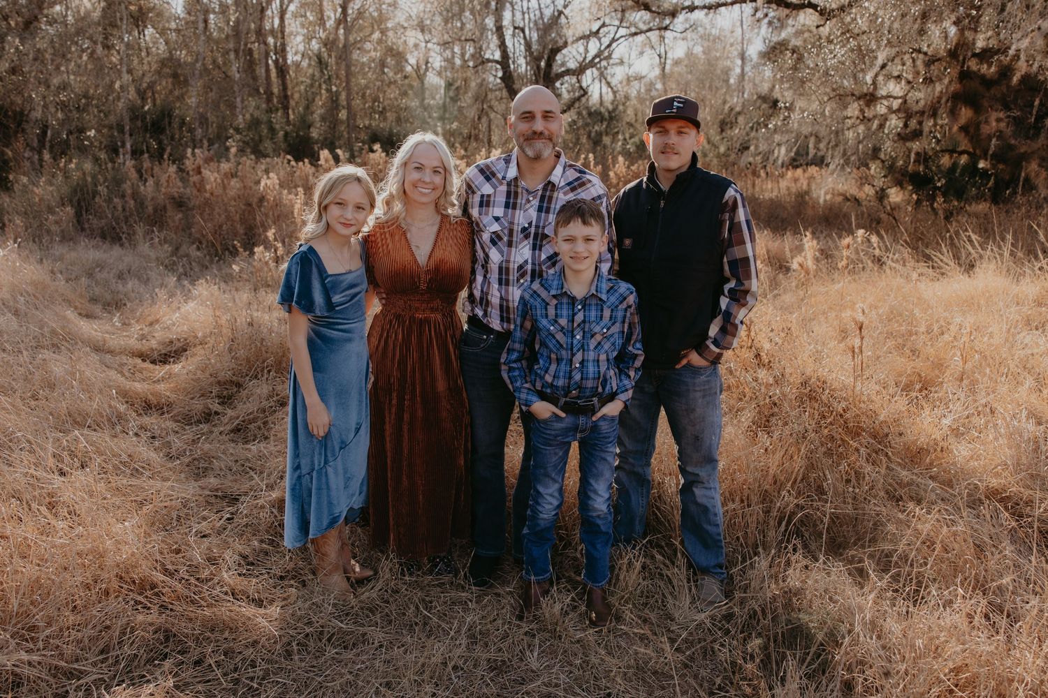 Family of four standing together in golden tall grass during sunset.