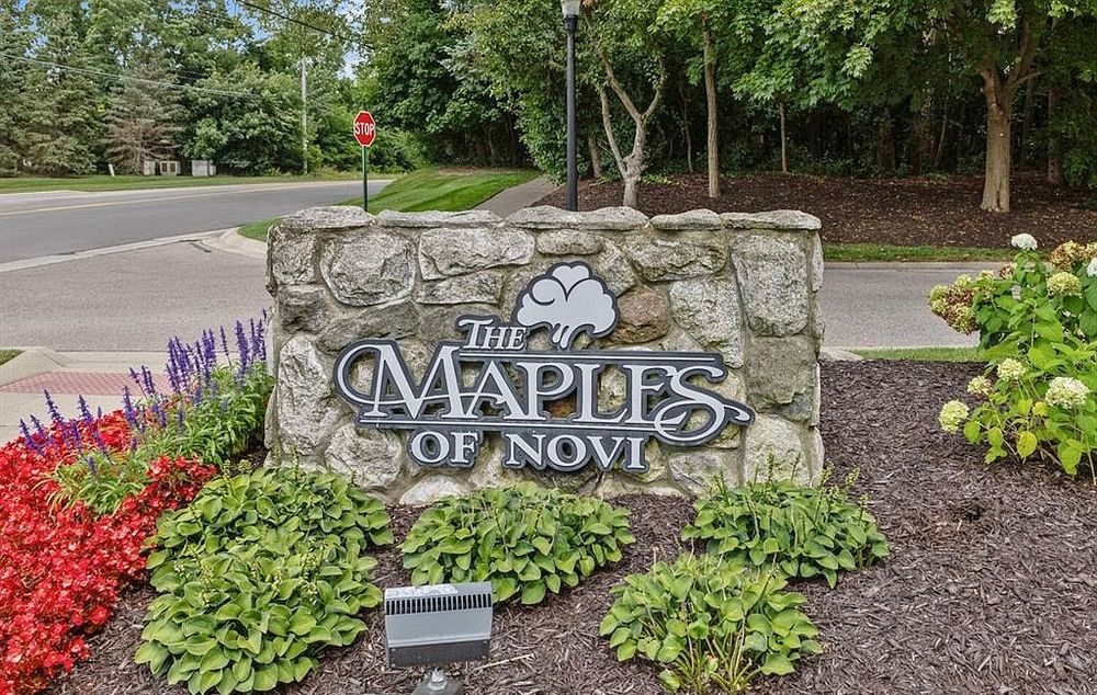 Stone entrance sign for The Maples of Novi community surrounded by colorful flowers and greenery.