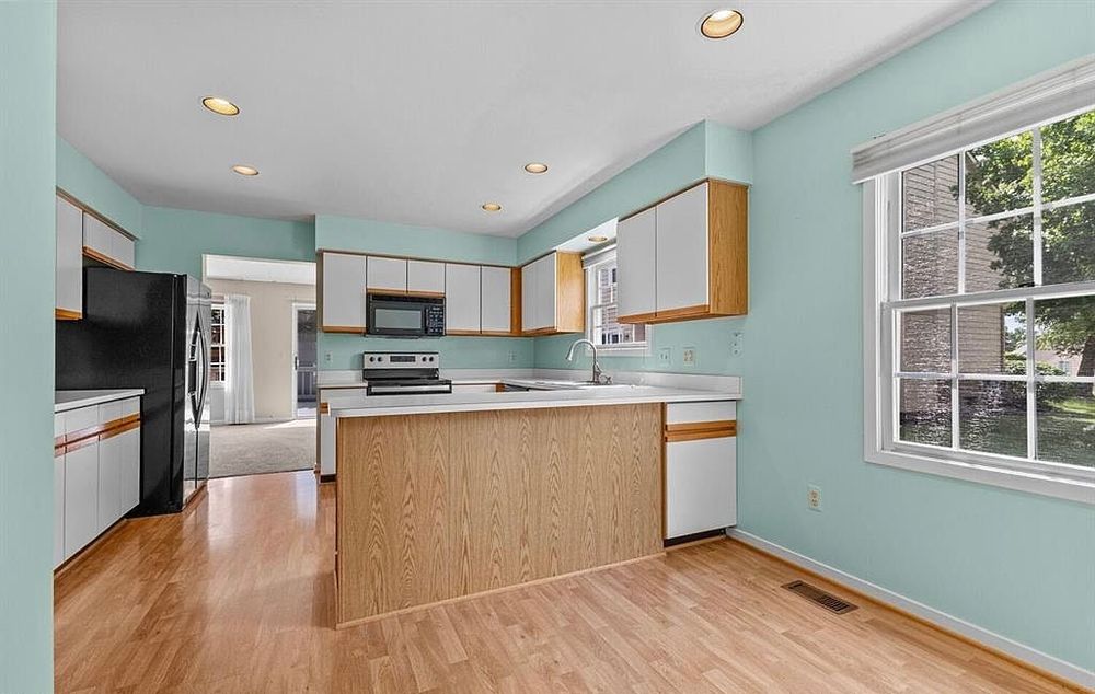 Open kitchen layout with peninsula island, white cabinets, hardwood floors, mint green walls, and view into adjacent living area.