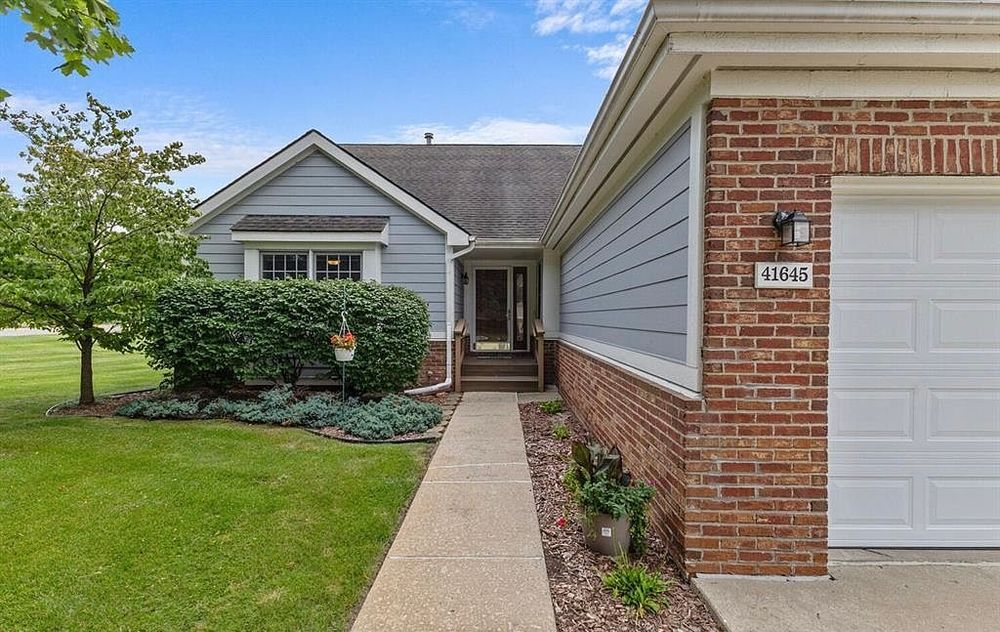 Close-up of a brick and gray vinyl ranch home entrance with a landscaped walkway and address number.