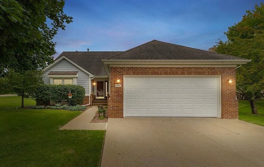 Twilight view of a brick and gray vinyl ranch home with two-car garage and landscaped front yard.